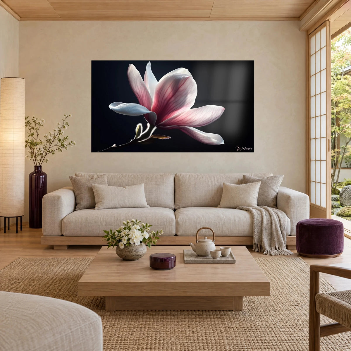 Wall art of a pink and white magnolia flower backlit on a black background, above a sofa in a bright living room