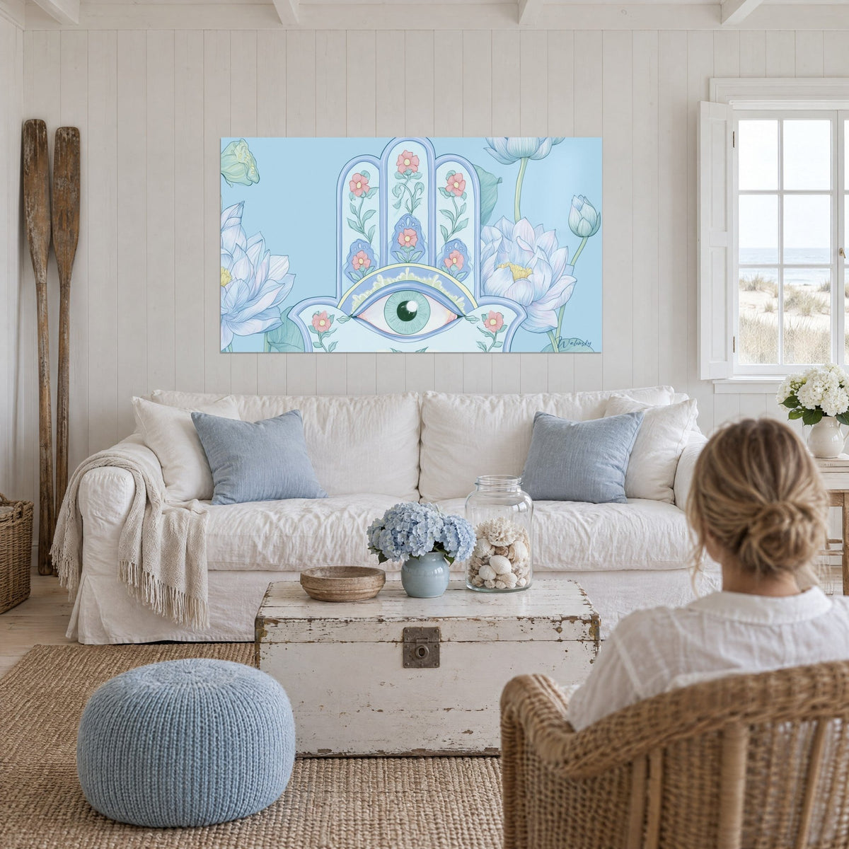 Cuadro mano de Fatma con pétalos de nenúfar azul pastel y flores rosas, ojo verde almendra, encima de un sofá en un salón luminoso
