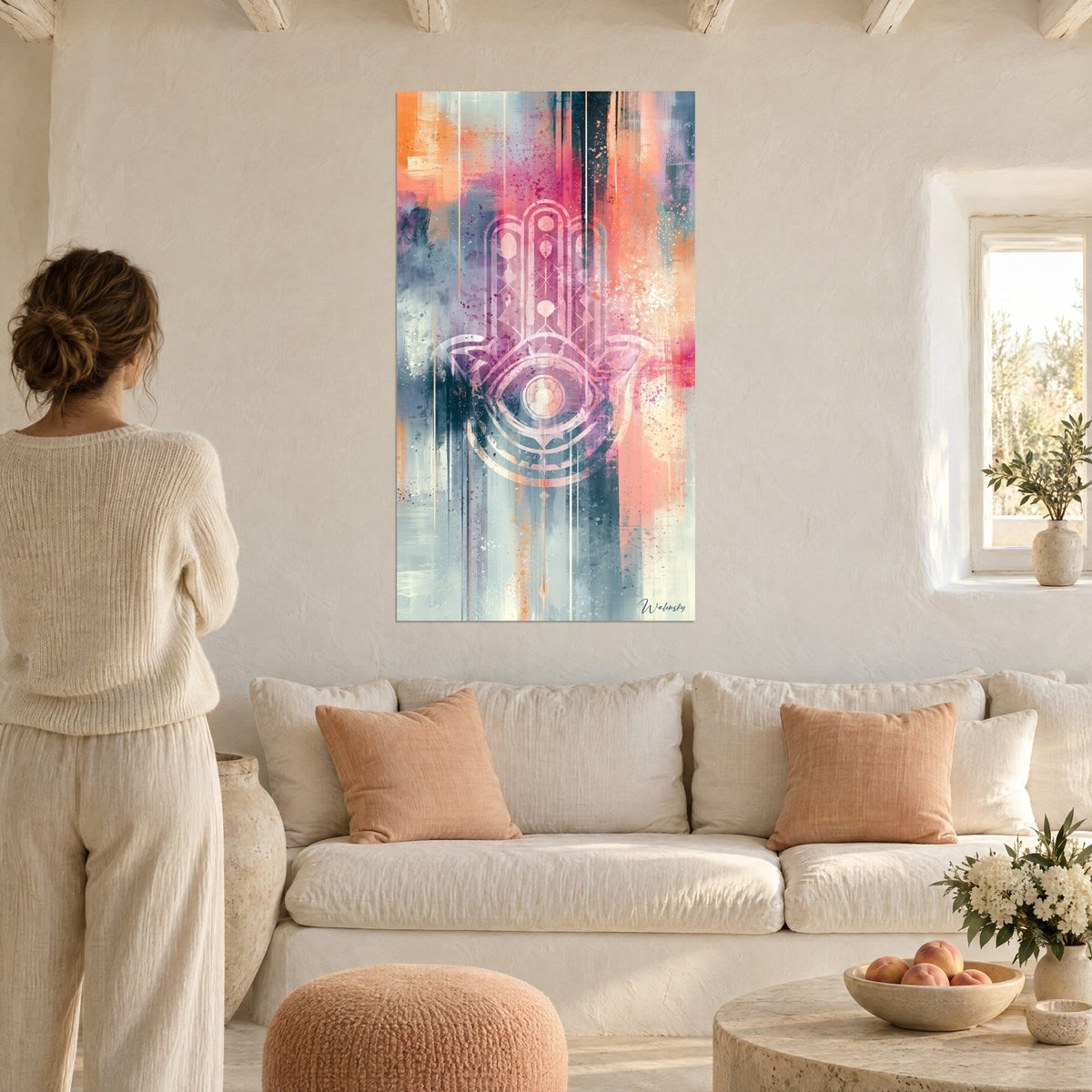 Wall art with a Fatma hand in pale pink patterns on a coral and grey background, woman seen from behind, above a sofa in a bright living room