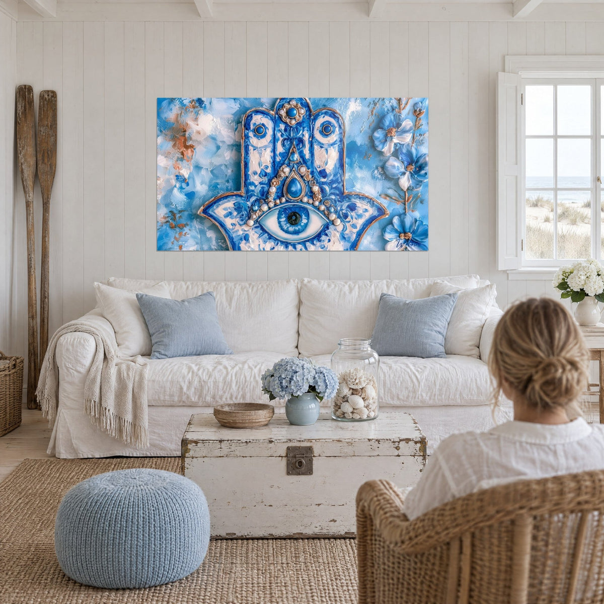 Tableau amulette hamsa bleu cobalt et blanc, œil central et perles nacrées, au-dessus d'un canapé dans un salon lumineux