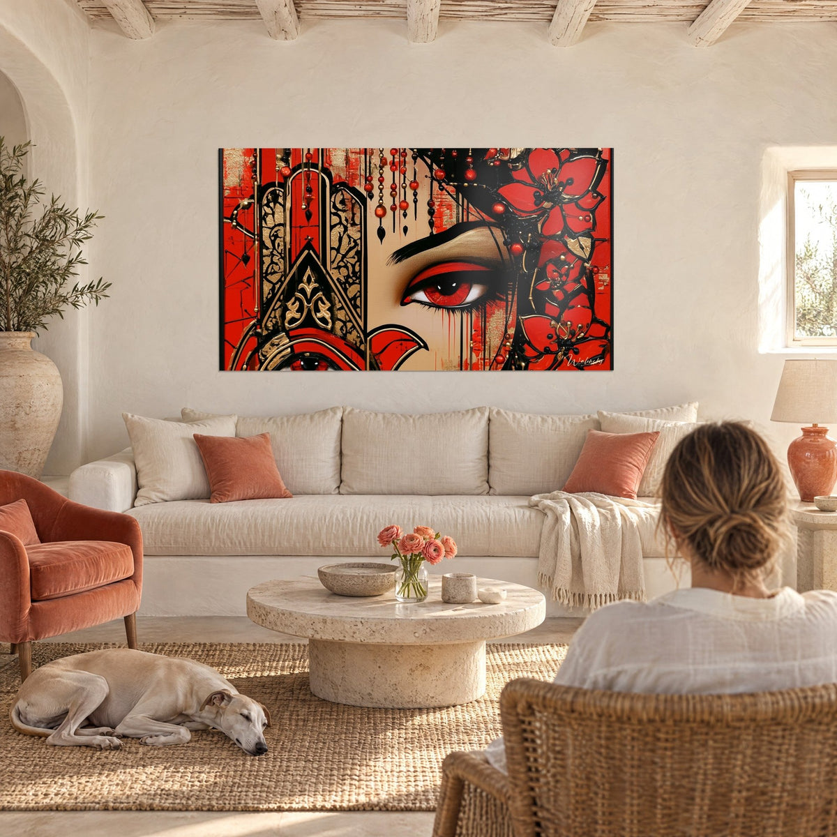 Tableau œil rouge sertissant un regard voilé, main de fatma dorée et fleurs noires, au-dessus d'un canapé dans un salon lumineux