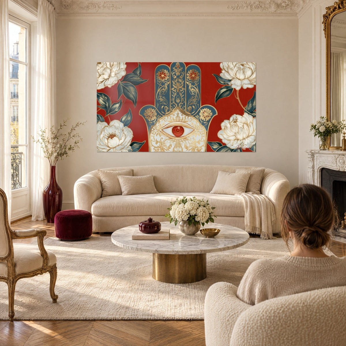 Tableau main de Fatma bleu marine aux filets dorés, œil ambré sur fond rouge, pivoines ivoire, au-dessus d'un canapé dans un salon lumineux
