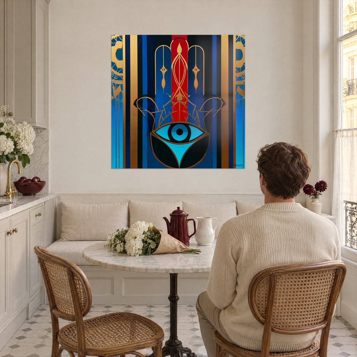 Gemälde Hamsa-Symbol in Königsblau und Rot, goldene Arabesken, betrachtet von einem Mann mit dem Rücken zum Betrachter, der in einer Haussmann-Küche am Tisch sitzt