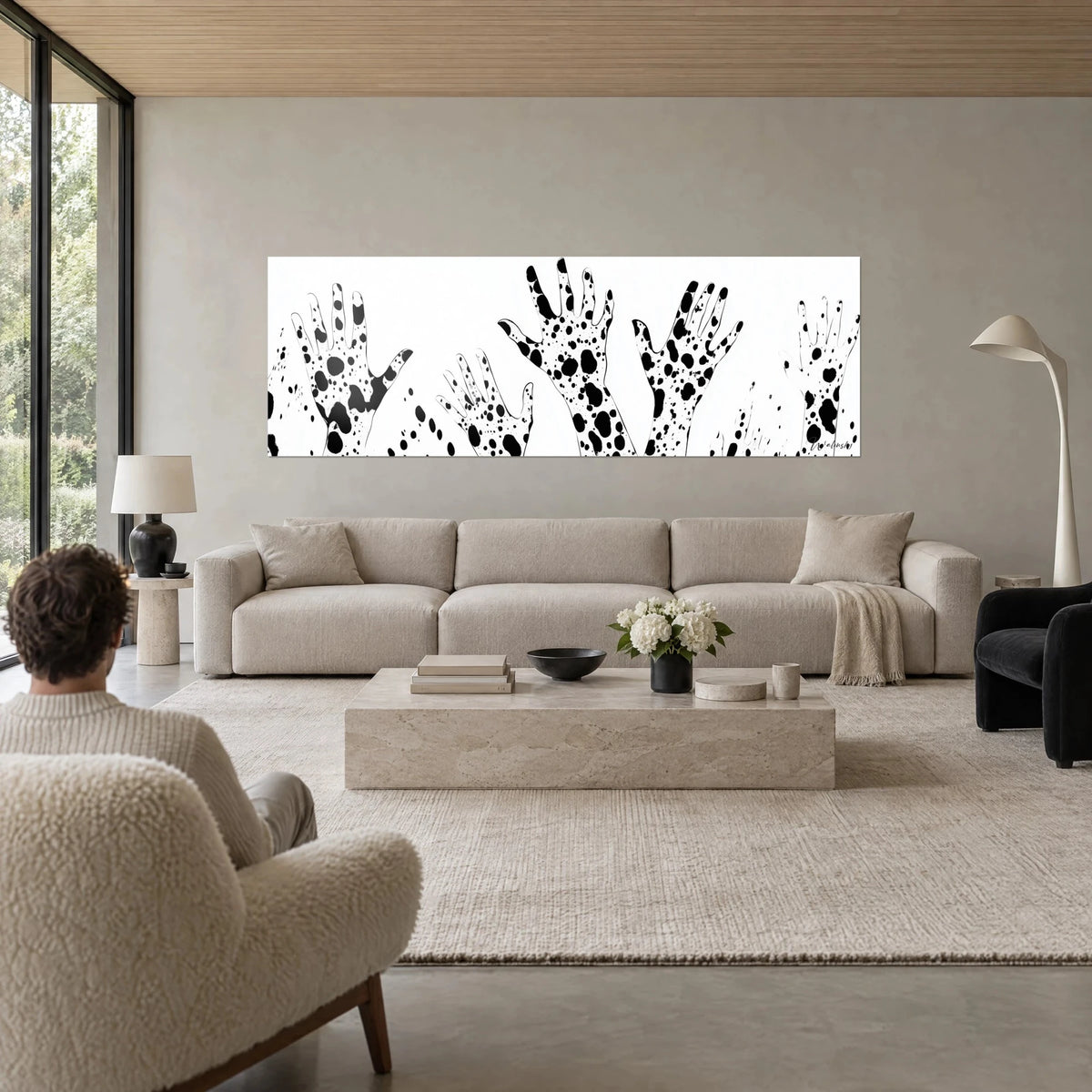 Tableau mains levées tachetées noir sur fond blanc, personne de dos, au-dessus d'un canapé dans un salon lumineux