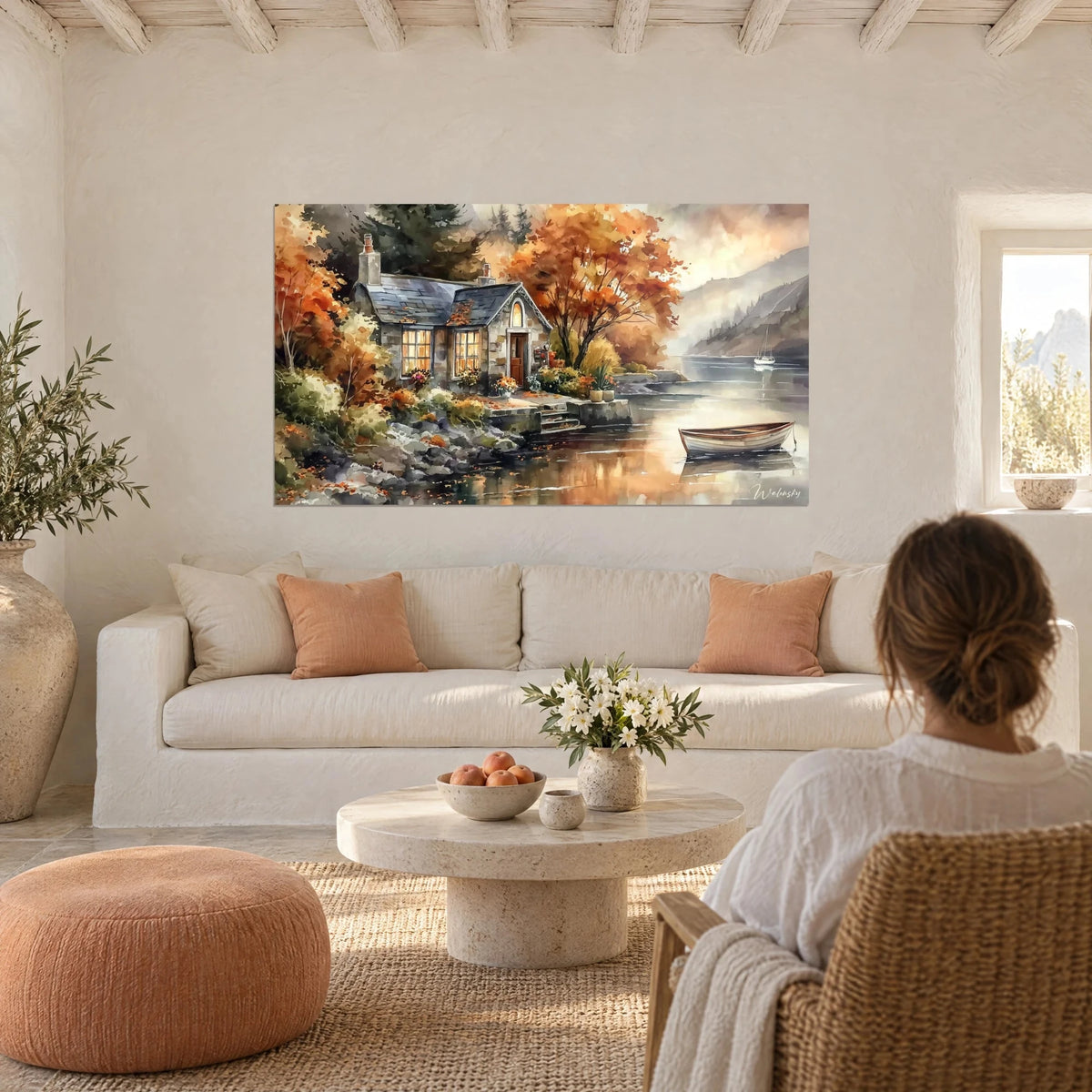 Wall art stone cottage with amber-lit windows, orange maple and ivory boat on grey lake, above a sofa in a bright living room