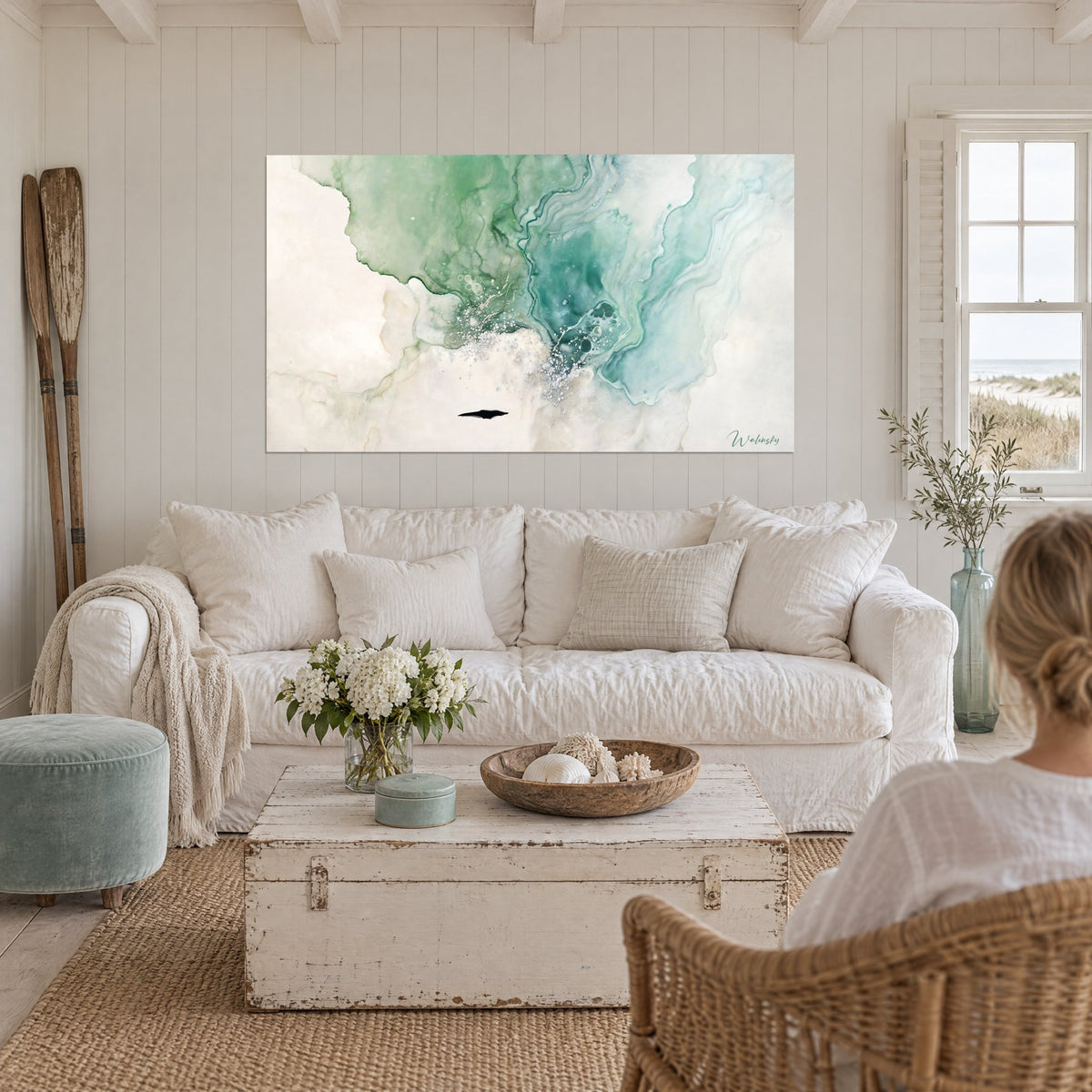 Tableau aquarelle fluide vert émeraude et turquoise sur fond crème, deux personnes de dos, au-dessus d'un canapé dans un salon lumineux