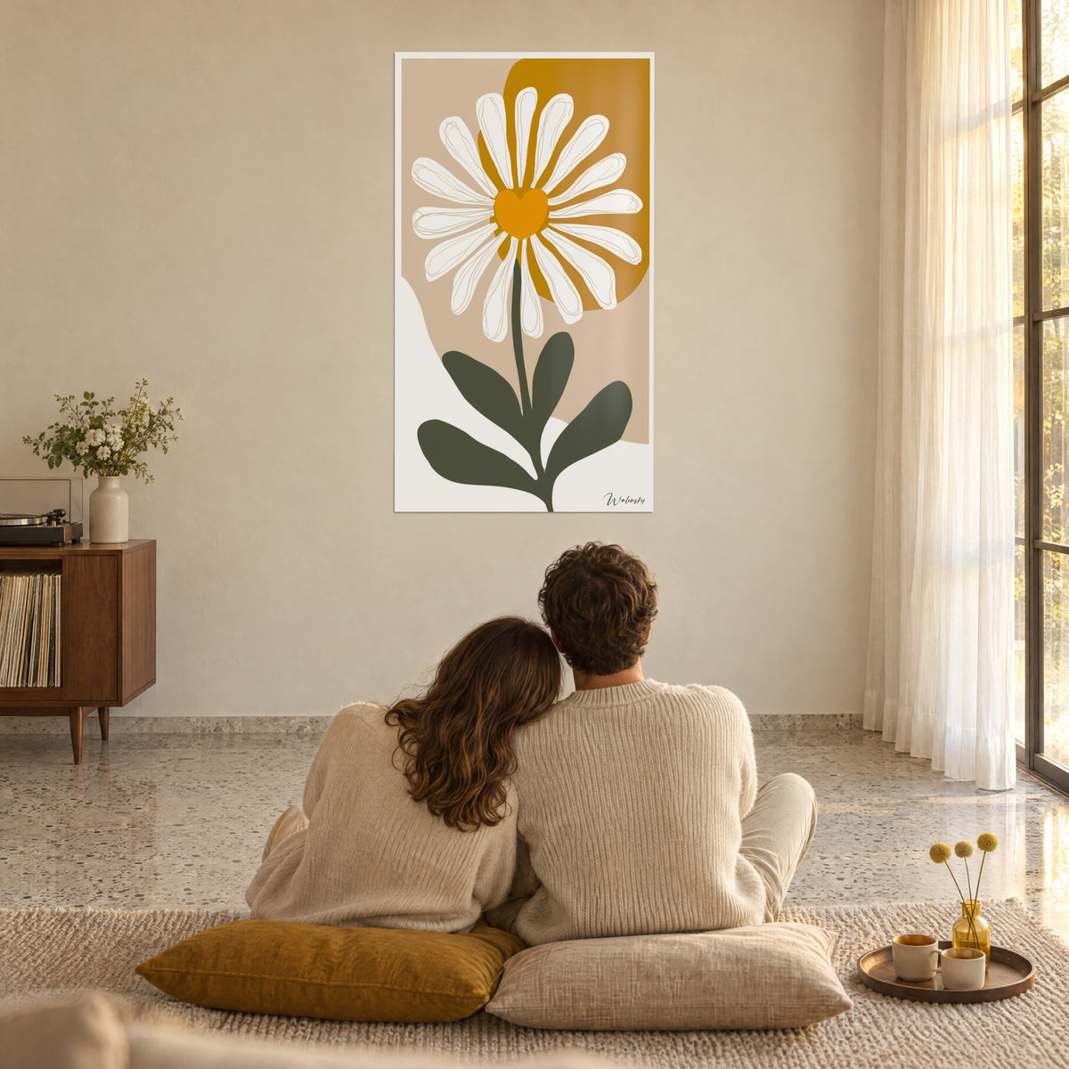 Cuadro de flor blanca con corazón naranja sobre un plano mostaza y beige, pareja de espaldas sentada sobre cojines mostaza, salón bañado de luz