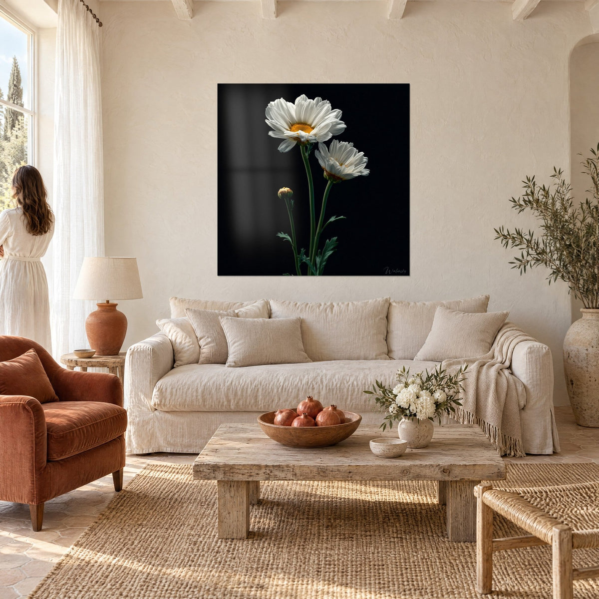 Wall art white daisies with orange centers on black background, woman in a light dress seen from behind, above a sofa in a bright living room