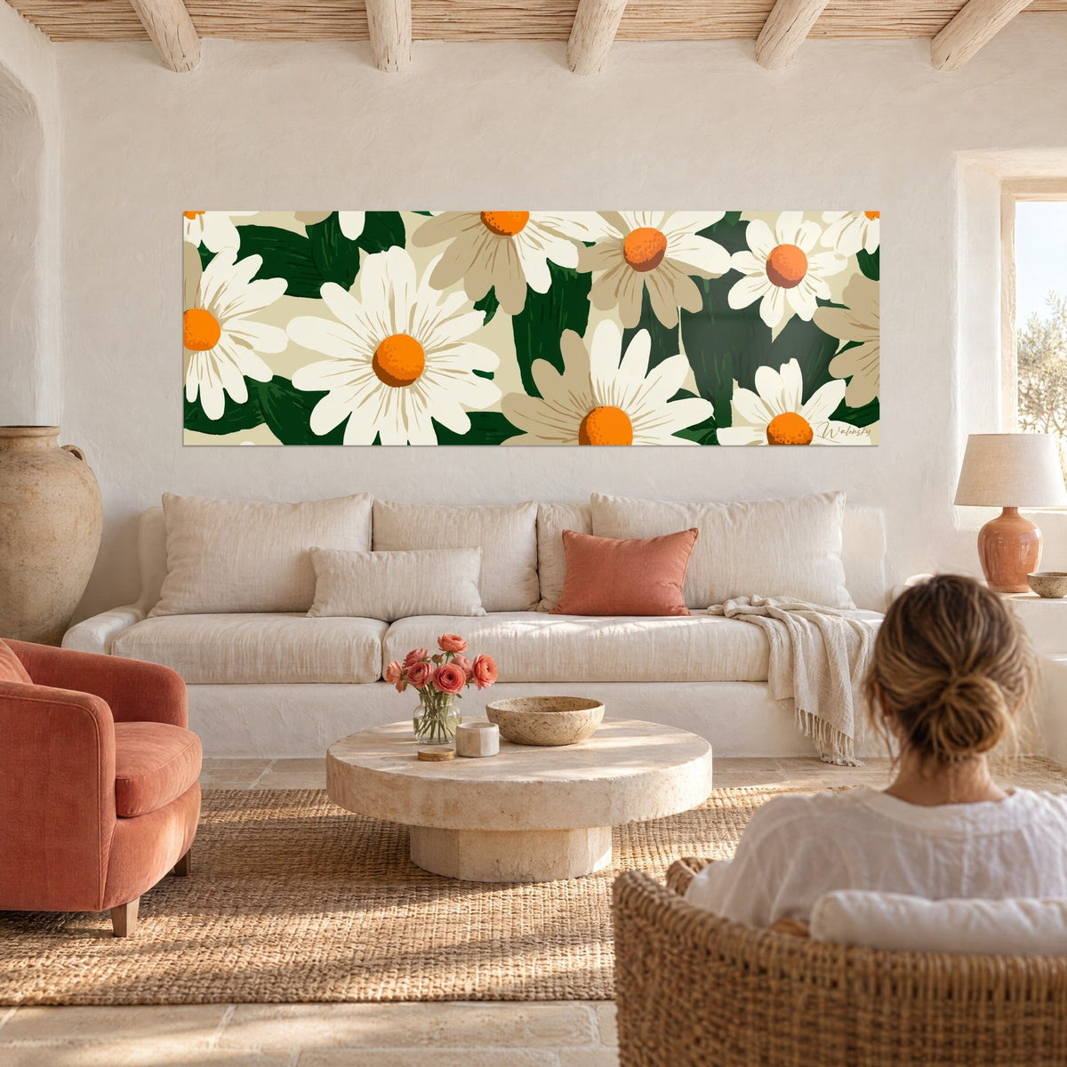 Tableau marguerites blanches aux cœurs orange vif sur feuillage vert sapin, une femme de dos, au-dessus d'un canapé dans un salon lumineux