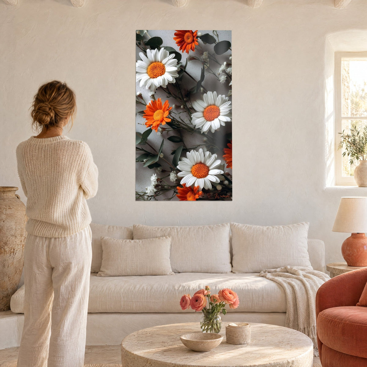 Cuadro margaritas blancas de corazón naranja sobre fondo gris moteado, mujer de espaldas, encima de un sofá en un salón luminoso