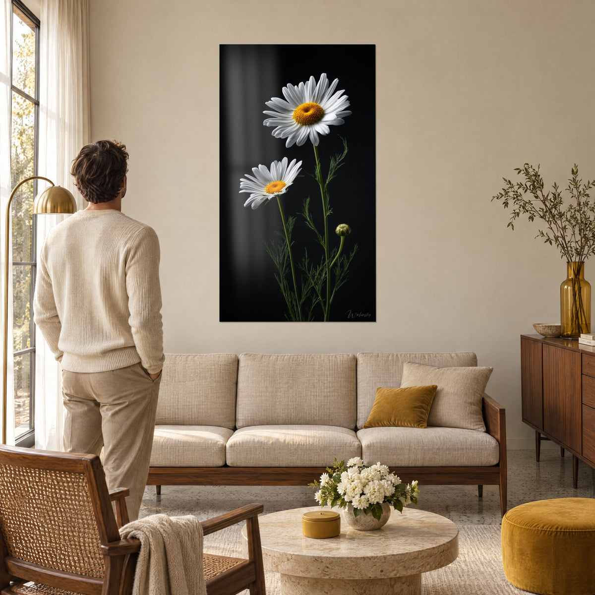 Tableau deux marguerites blanches au cœur jaune sur fond noir, un homme de dos, au-dessus d'un canapé dans un salon lumineux