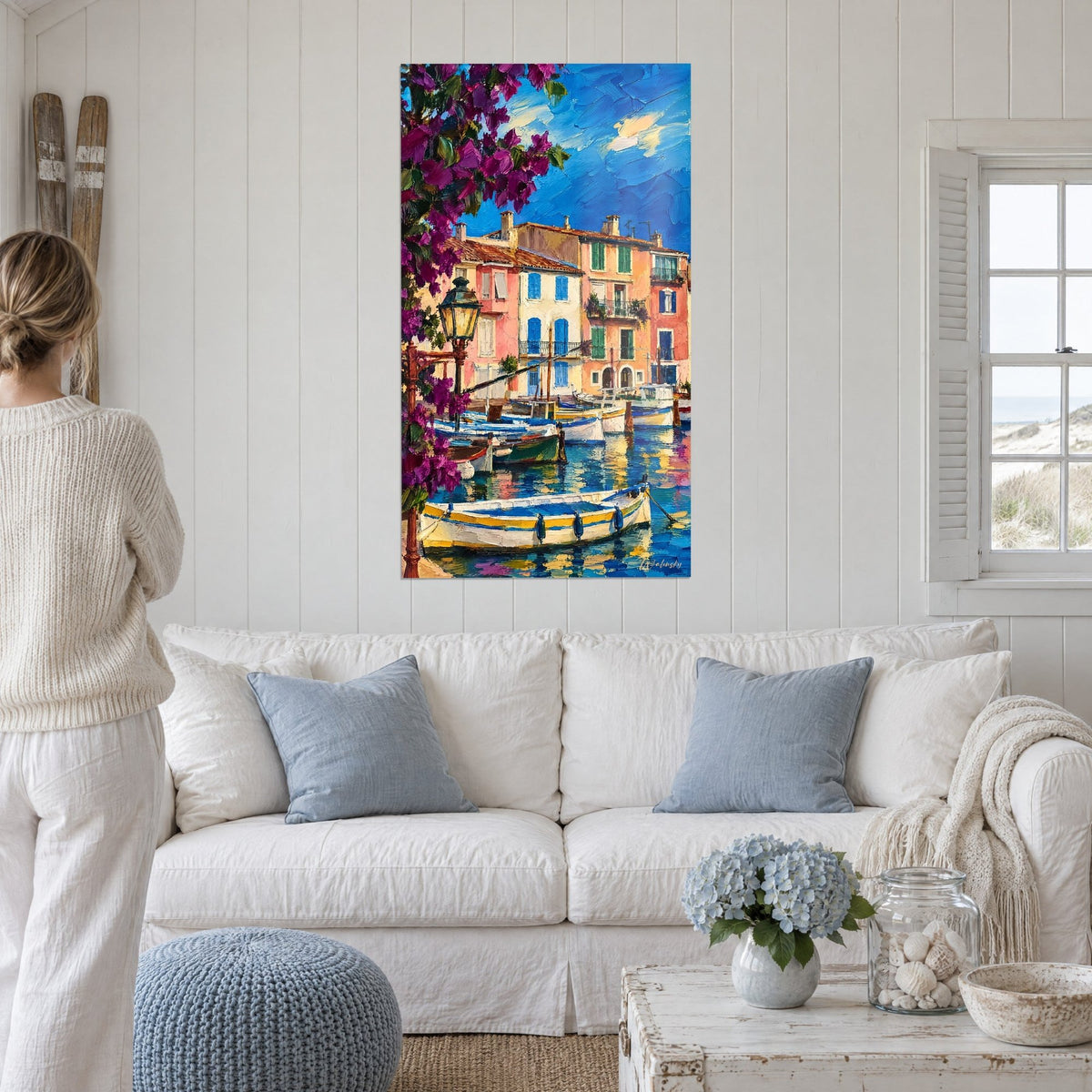 Tableau bougainvillier mauve devant façades roses et volets bleus, barques blanches sur l'eau, au-dessus d'un canapé dans un salon lumineux