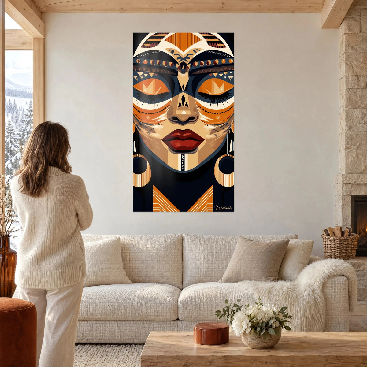 Tableau masque africain aux paupières closes, fard orange et bleu nuit, lèvres rouges, sous le regard d'une femme, au-dessus d'un canapé dans un salon lumineux