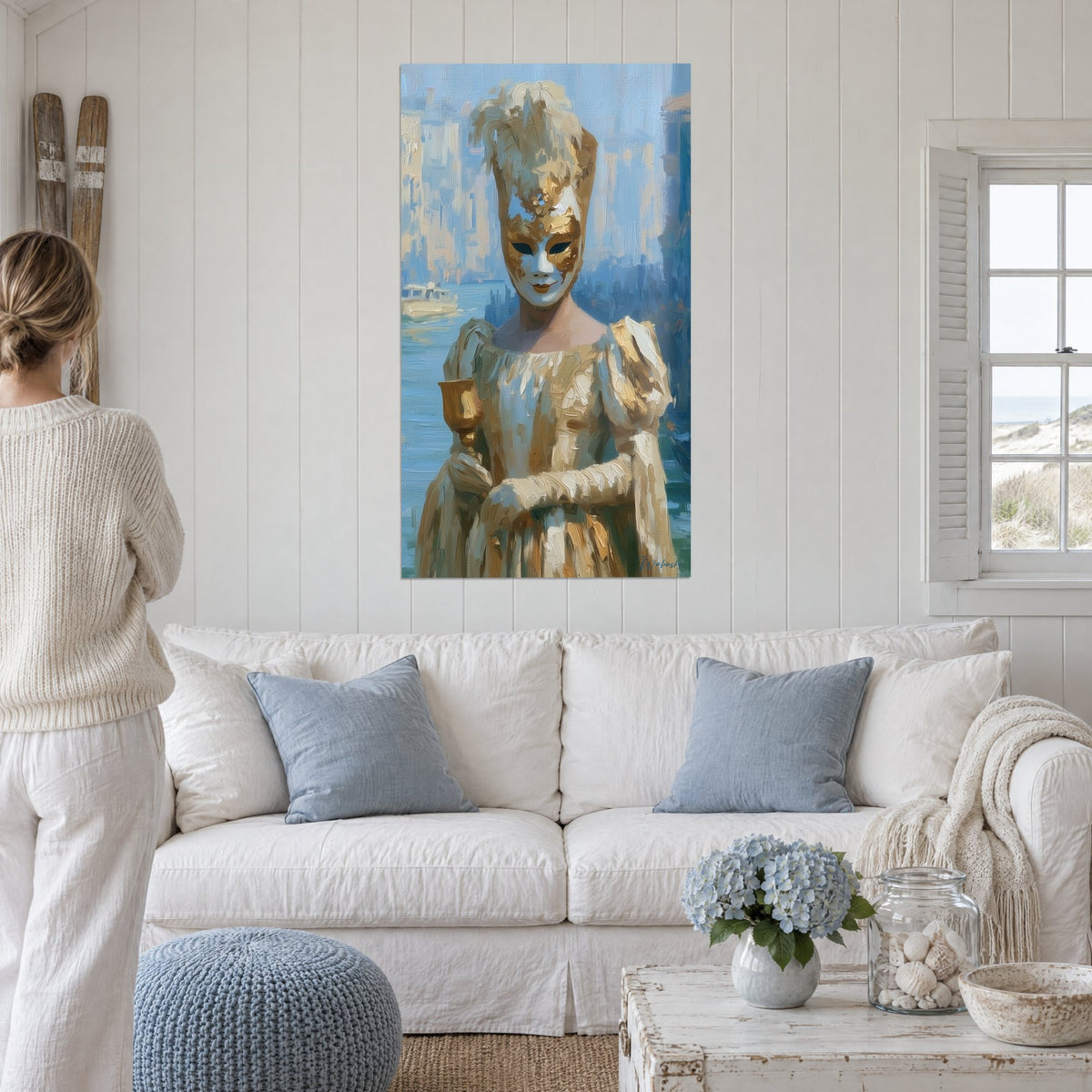 Quadro maschera veneziana bianca e oro che tiene un calice dorato, canale blu, sopra un divano in un soggiorno luminoso