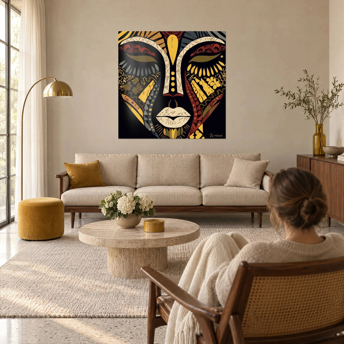 Tableau masque africain stylisé, visage noir aux arcs ivoire et rayons jaune moutarde, au-dessus d'un canapé dans un salon lumineux
