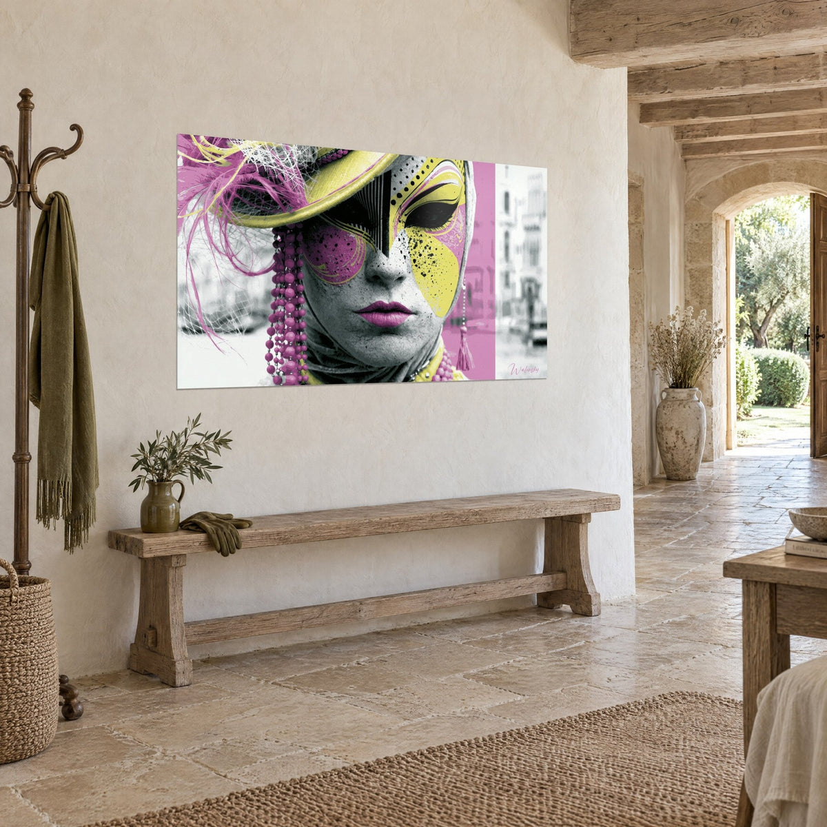 Quadro volto mascherato con motivi gialli e rosa, rete bianca e labbra fucsia, su un muro di pietra chiara di casa di campagna