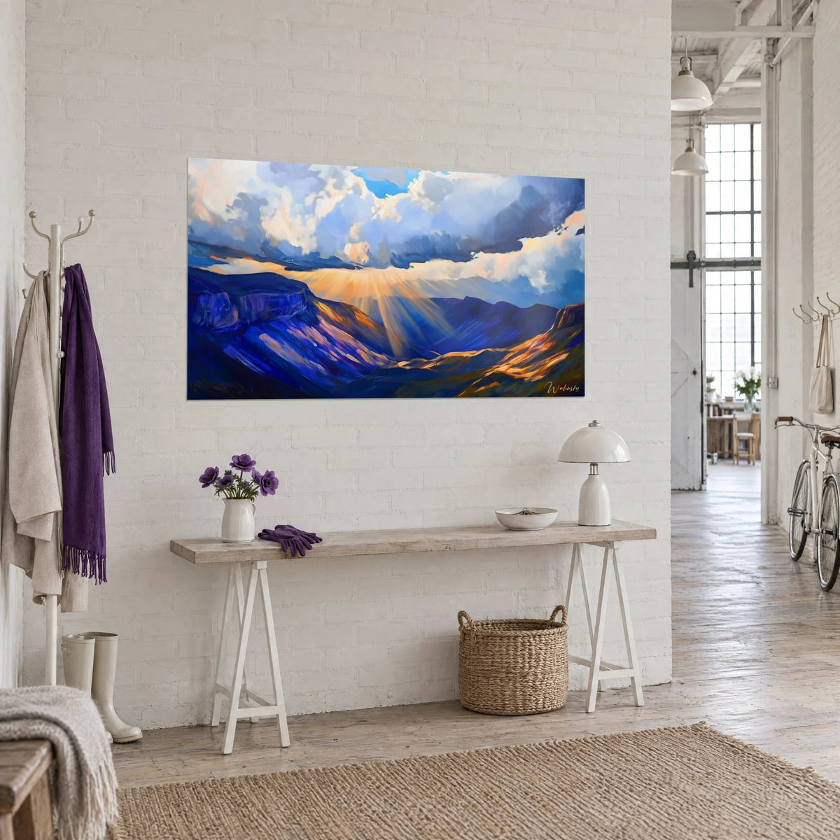 Tableau vallée de montagne baignée de rayons dorés sous un ciel bleu et blanc, accroché au-dessus d'une console en bois