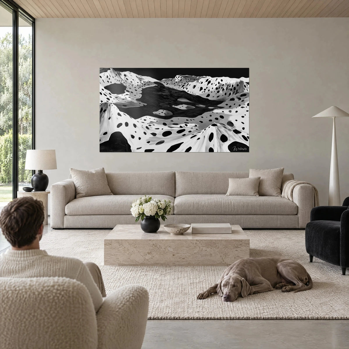 Wall art black and white speckled moon relief, dark ink lake between dotted ridges, above a sofa in a bright living room