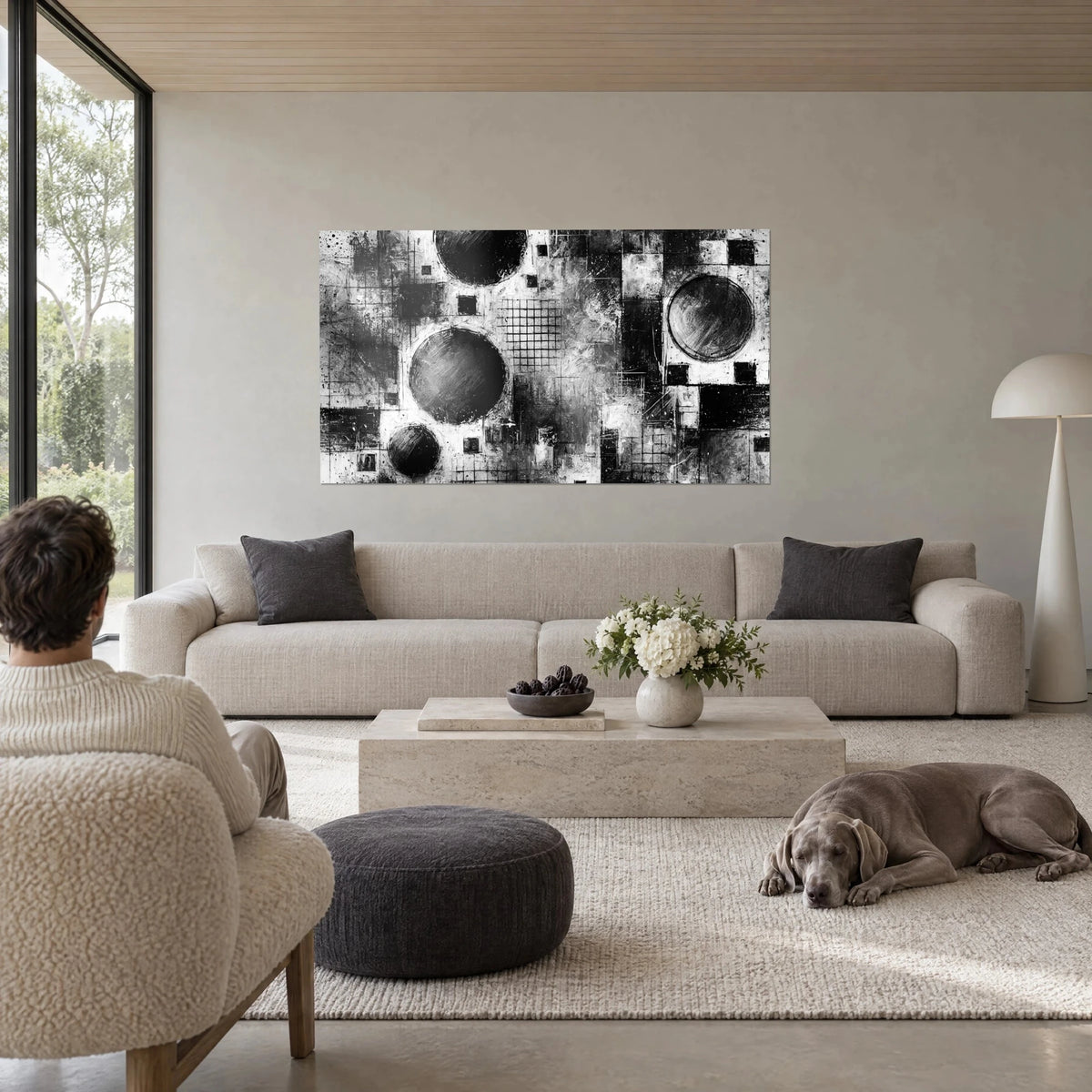 Wall art abstract composition of large black discs and grey grids on a white background, above a sofa in a bright living room