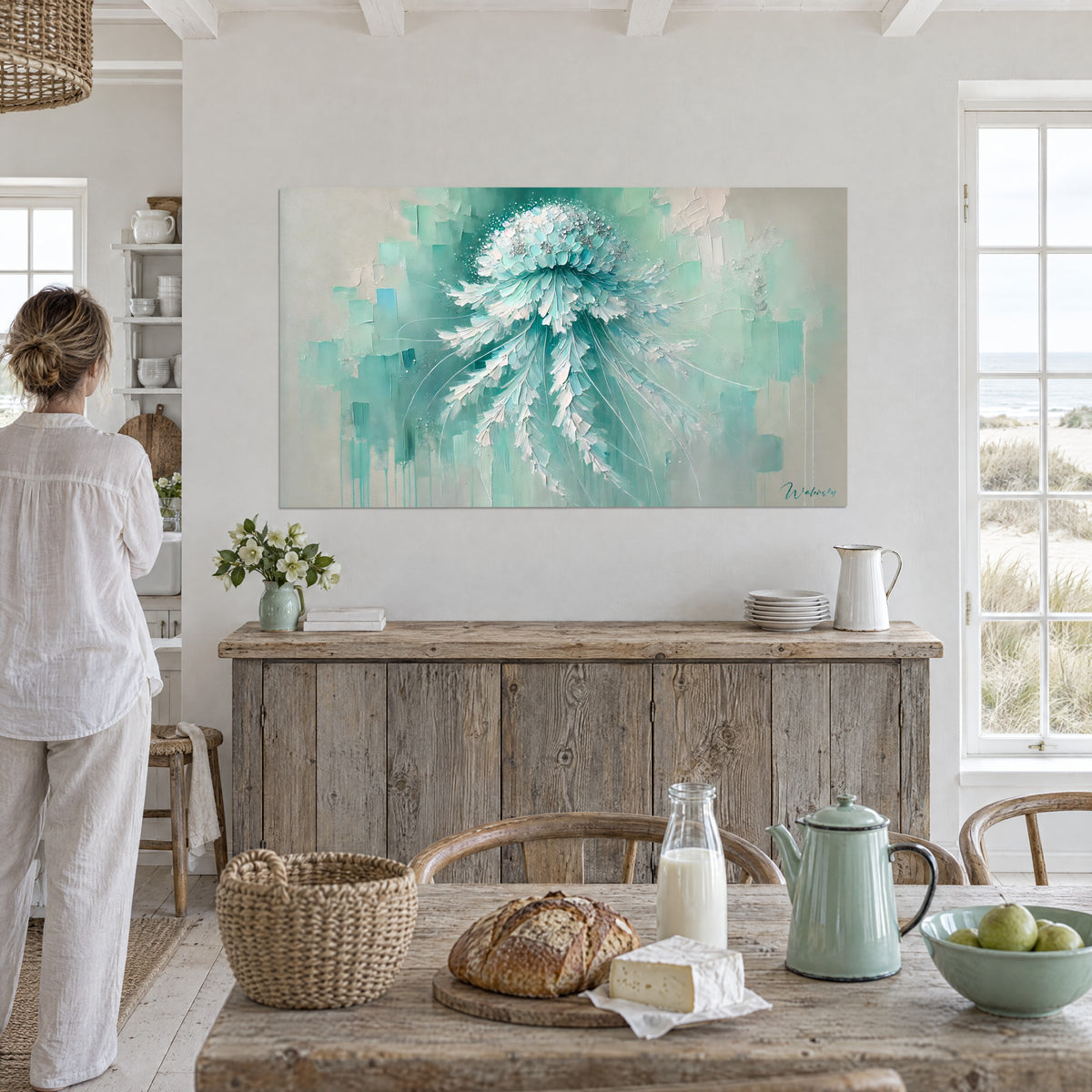 Wall art sparkling jellyfish in turquoise and pearl grey flat tones, daylight, a woman seen from behind beside a whitewashed wooden sideboard