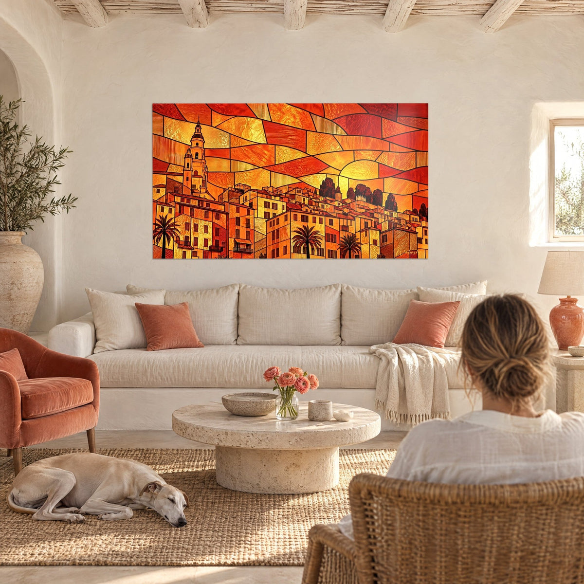 Tableau village côtier en vitrail ocre et rouge, clocher doré, deux personnes de dos et un lévrier, au-dessus d'un canapé dans un salon lumineux