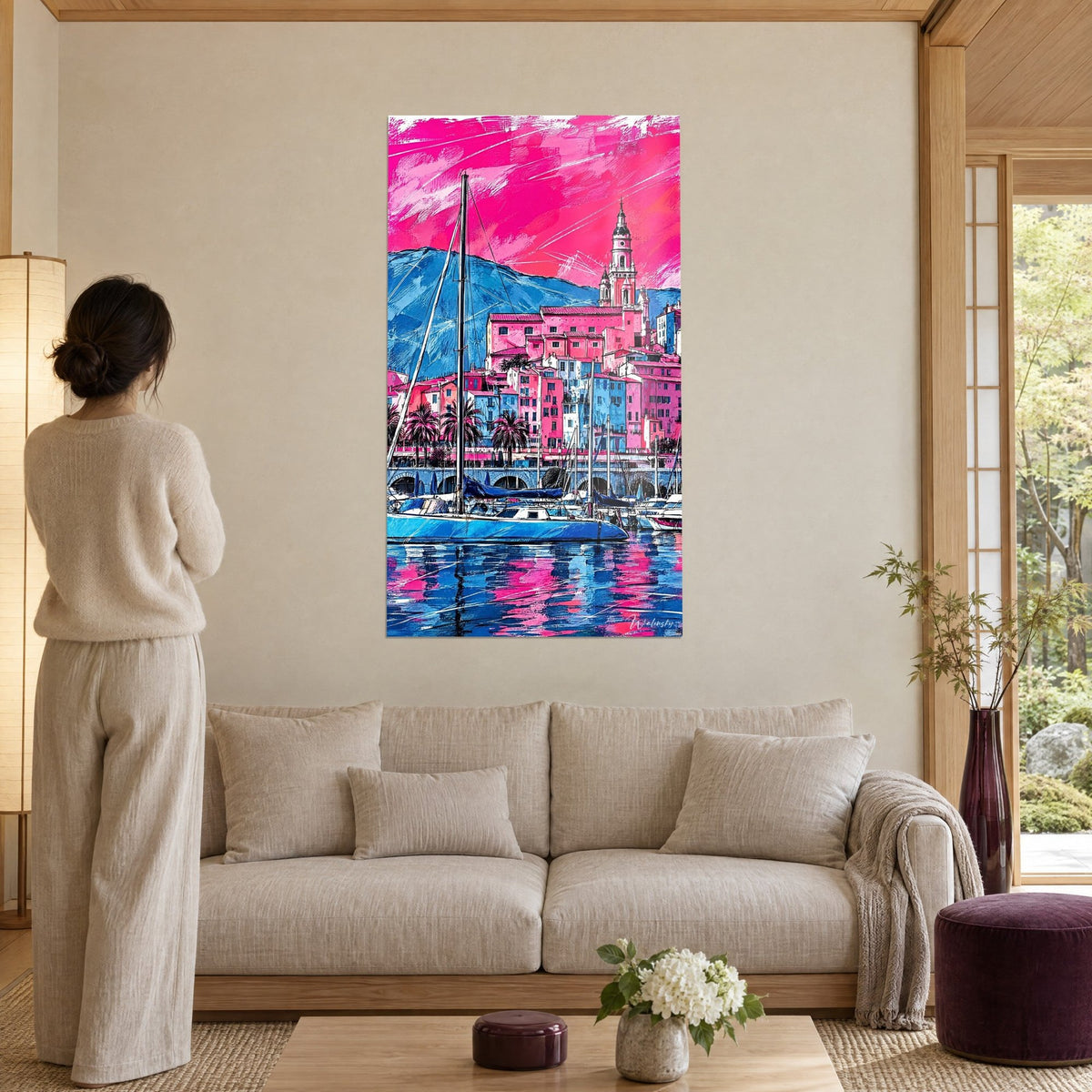Tableau port de Menton aux façades roses et clocher baroque, ciel fuchsia, coque bleue du voilier, au-dessus d'un canapé dans un salon lumineux