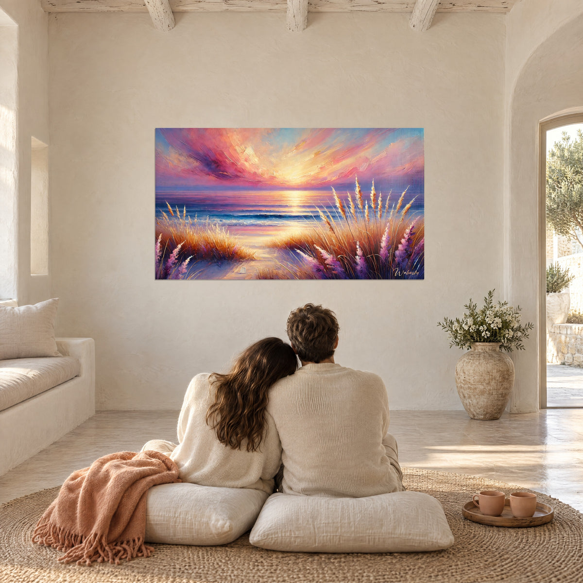 Tableau sentier de sable vers l'océan, ciel flamboyant rose et jaune, herbes cuivrées, contemplé par un couple de dos assis sur des coussins