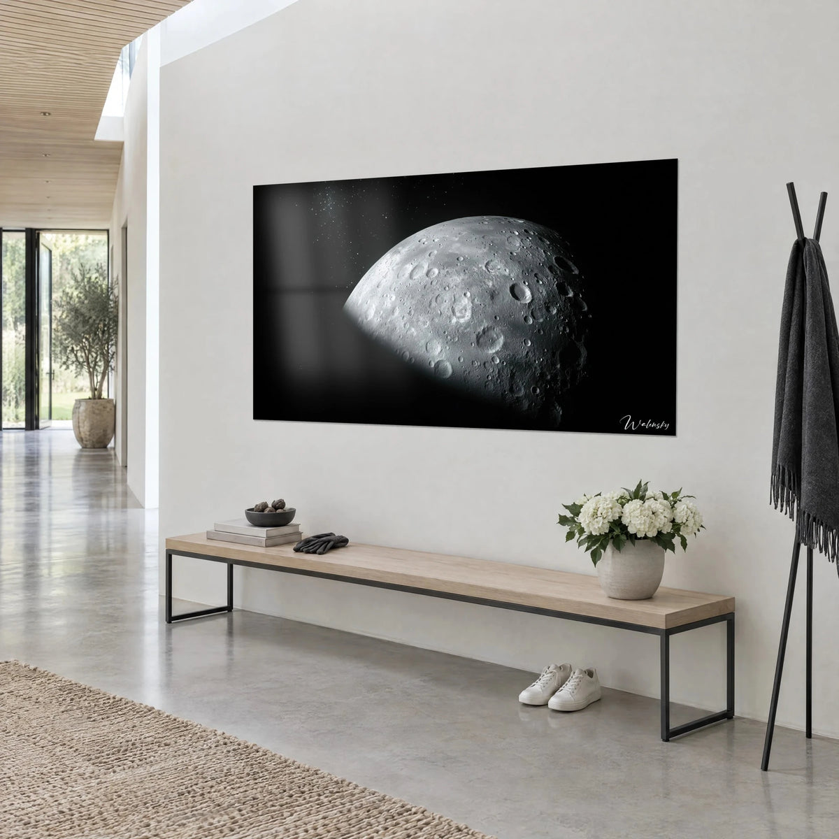 Cuadro de una esfera lunar gris salpicada de cráteres, reflejo sobre la pared blanca, banco de madera y estantería negra, vista de tres cuartos