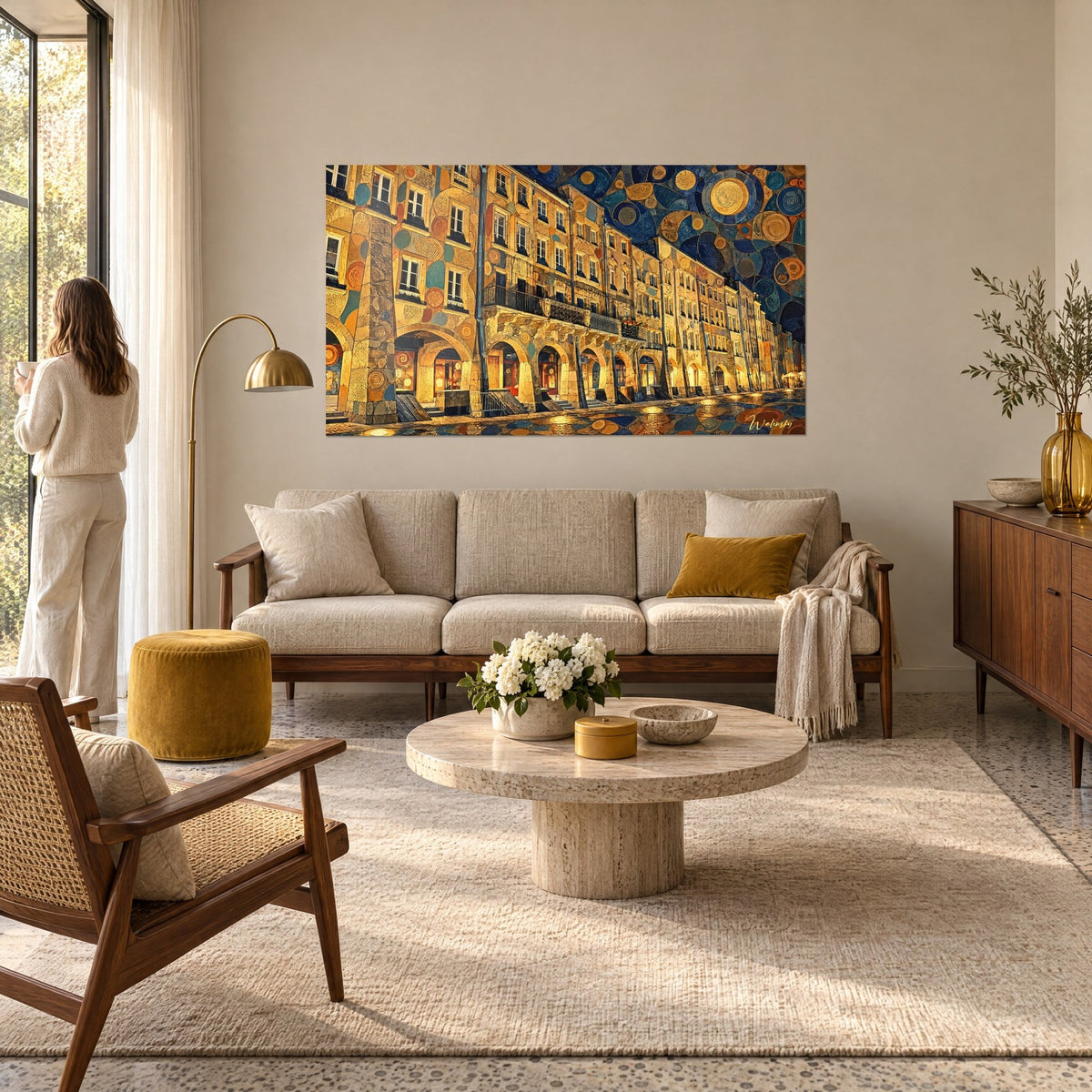 Wall art arcaded street with ochre stones and midnight blue circles, woman seen from behind facing the scene, above a sofa in a bright living room