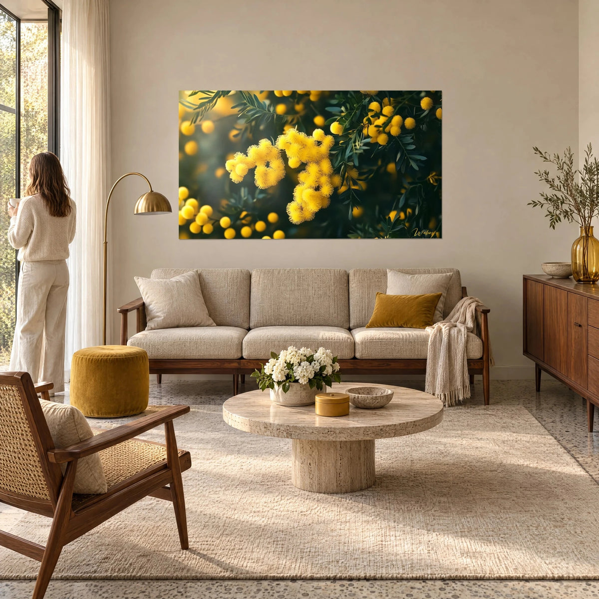 Wall art of yellow lemon mimosa clusters on dark green foliage, blurred golden background, above a sofa in a bright living room