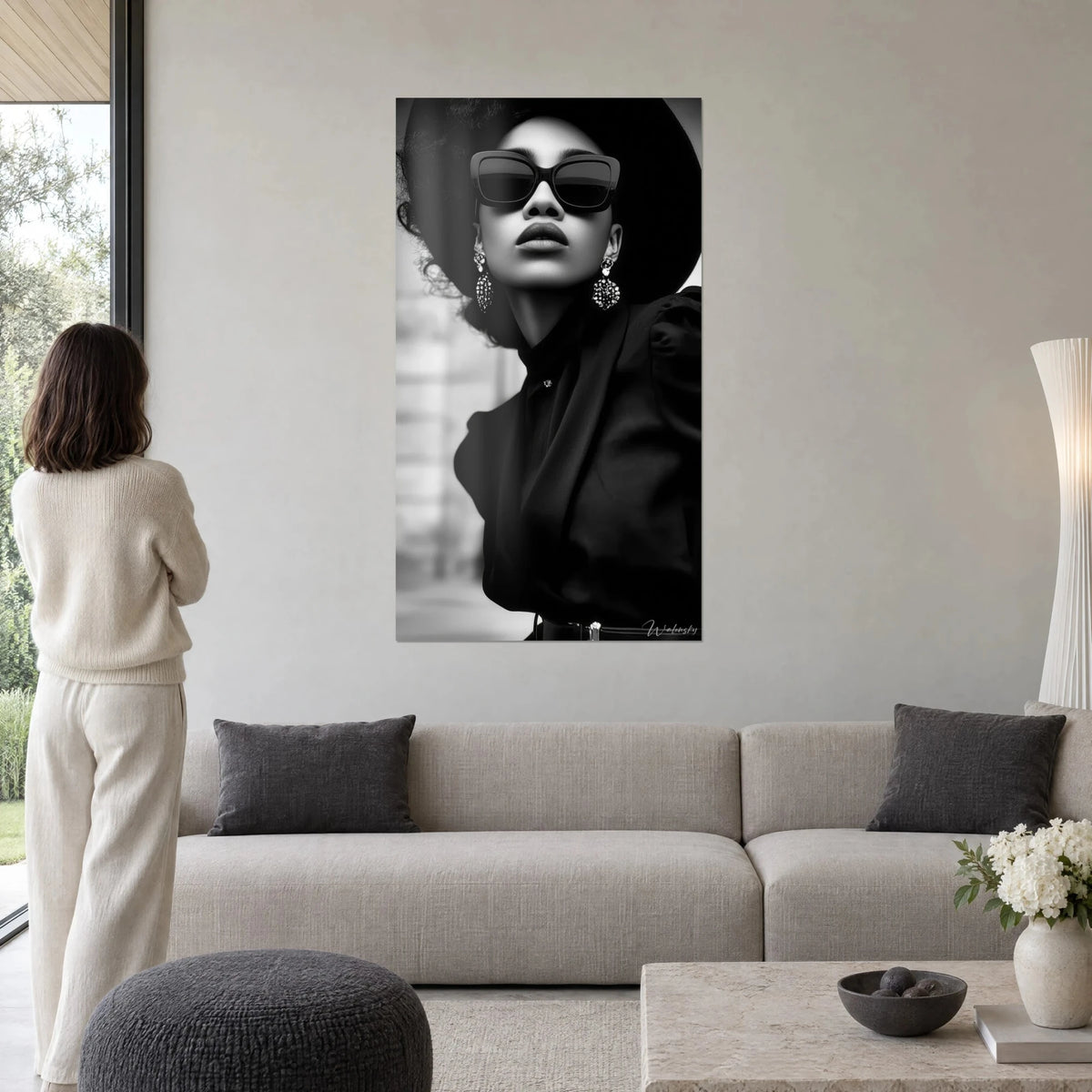 Tableau femme élégante en chapeau noir et lunettes carrées, boucles d'oreilles perlées, gris perle, au-dessus d'un canapé dans un salon lumineux
