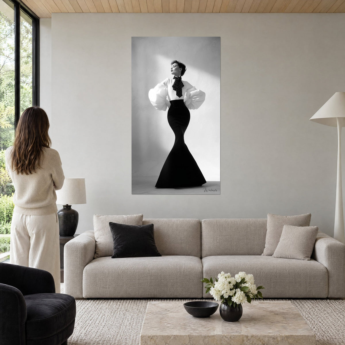 Quadro di una donna elegante in abito a sirena nero, maniche a sbuffo bianche e fiocco a pois, sopra un divano in un soggiorno luminoso