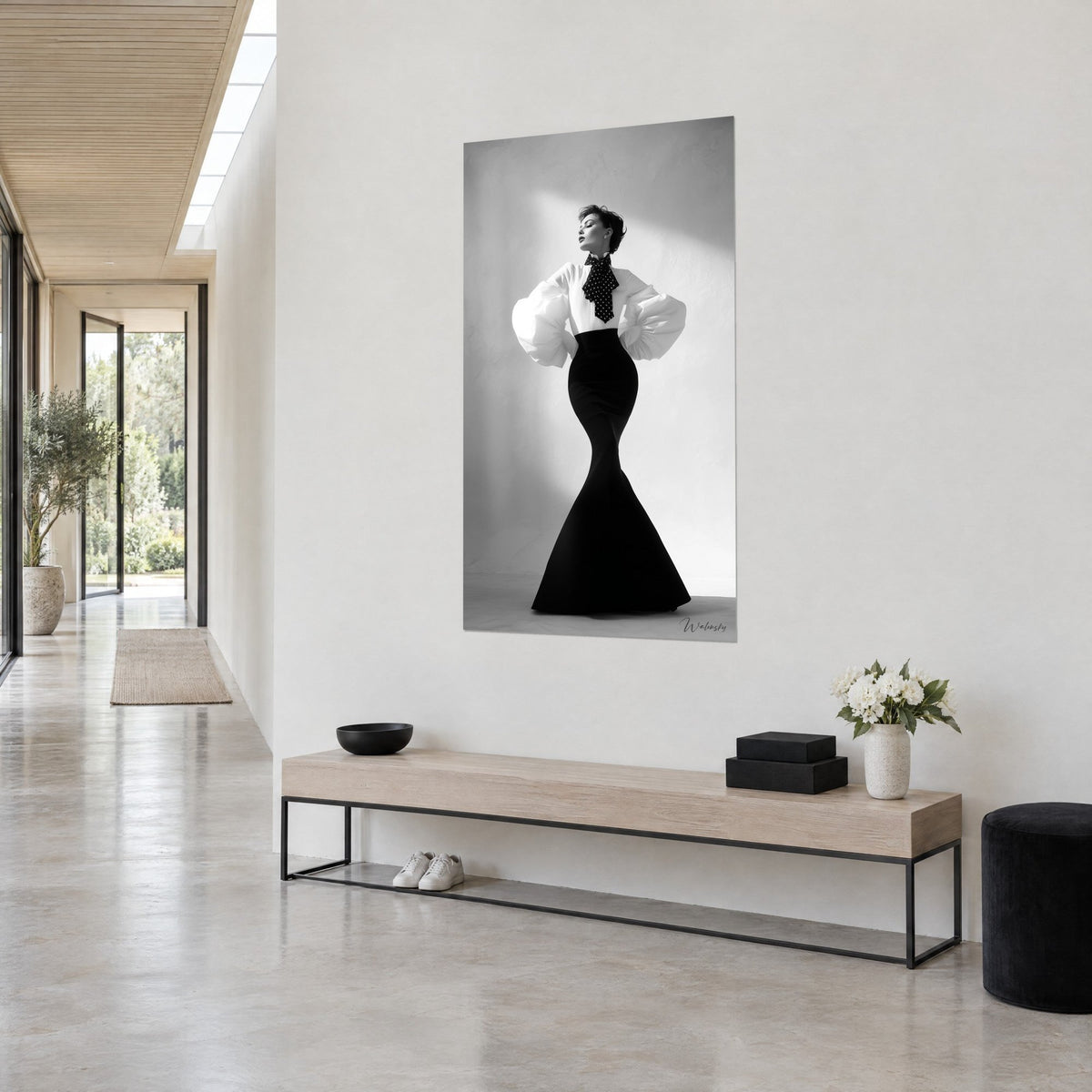 Quadro di una modella con foulard a pois al collo, gonna a sirena nera su fondo grigio chiaro, panca di legno in un corridoio