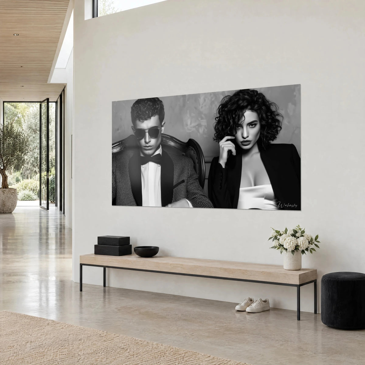 Quadro duo glamour in monocromo, abito principe di Galles e blazer nero su raso avorio, poltrona scultorea, parete beige in tre quarti