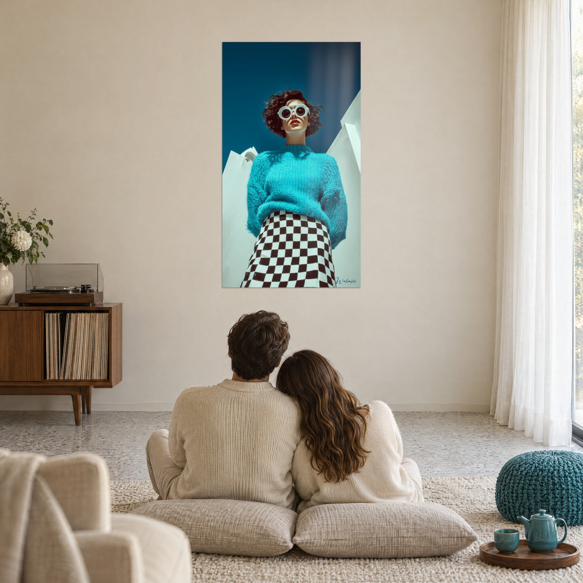 Wall art of a muse with oversized white glasses, fluffy turquoise knit, chocolate and ivory checkered pattern, facing a couple embracing on cushions