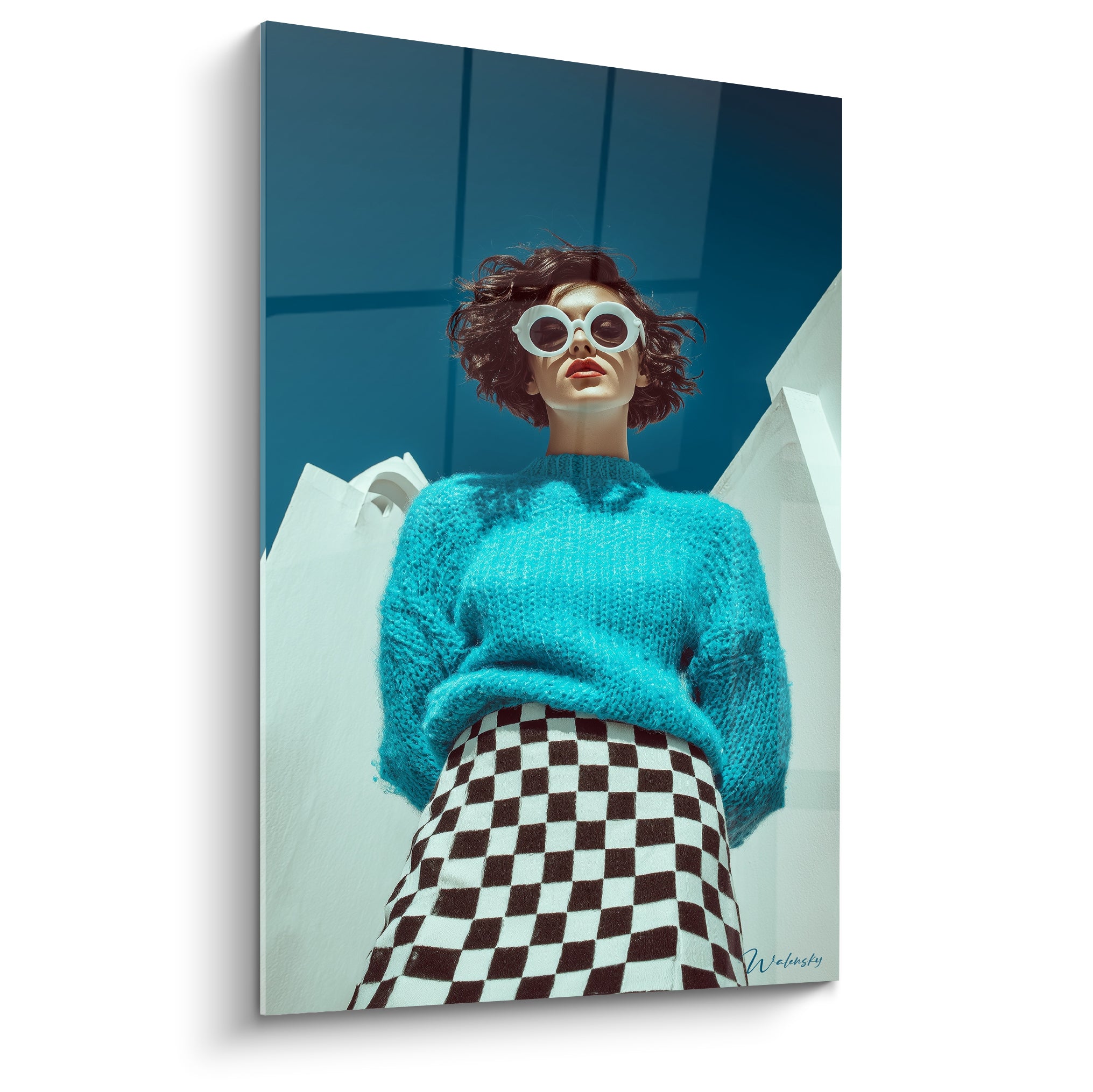 Femme aux lunettes rondes blanches, pull turquoise et jupe échiquier noir et blanc en contre-plongée