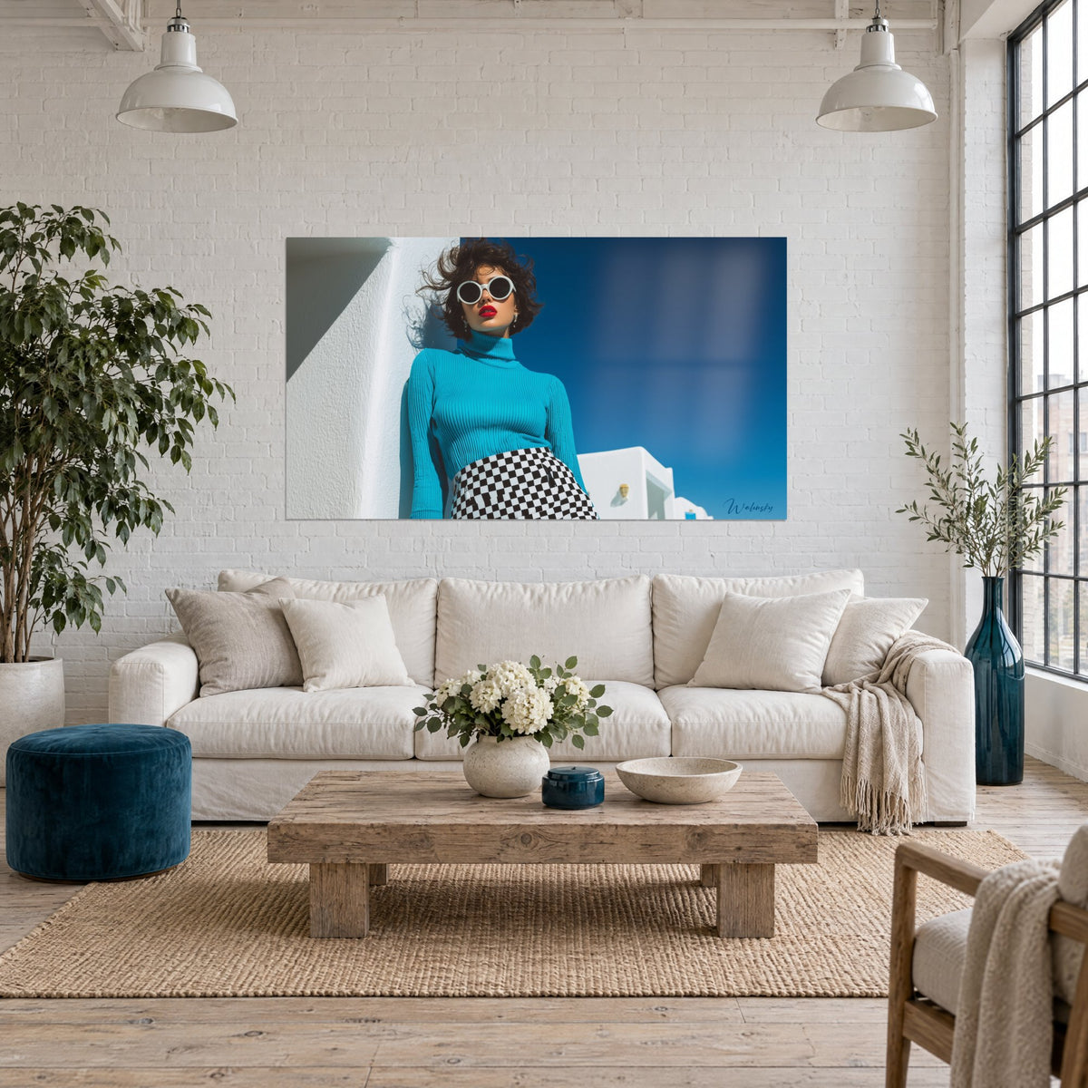 Tableau mannequin aux lunettes rondes blanches et lèvres rouges, pull turquoise, ciel bleu roi, au-dessus d'un canapé dans un salon lumineux