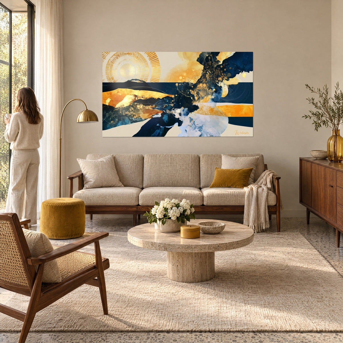 Wall art golden sun radiating over navy and cream waves, woman seen from behind, above a sofa in a bright living room