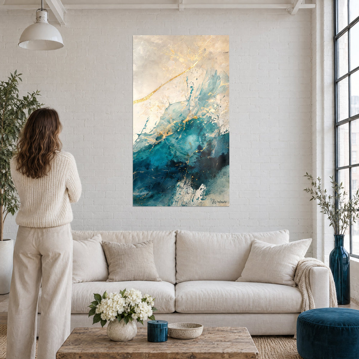 Tableau vague turquoise suspendue striée de veines dorées, femme de dos, au-dessus d'un canapé dans un salon lumineux