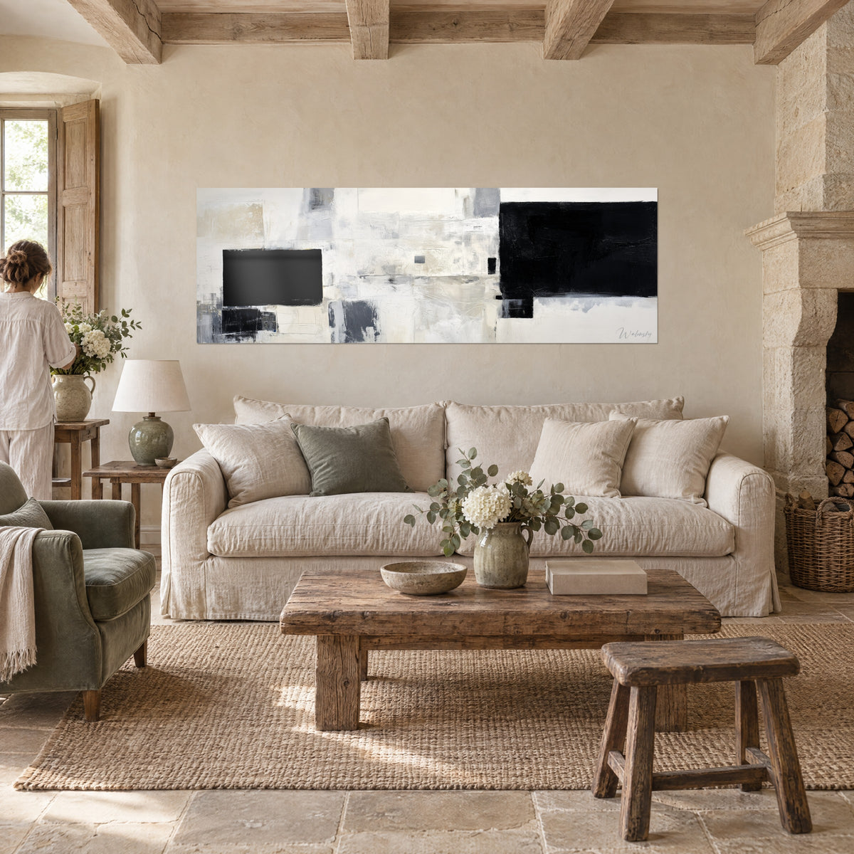 Wall art abstract with black blocks on cream white and pearl grey background, a woman seen from behind above a sofa in a bright living room