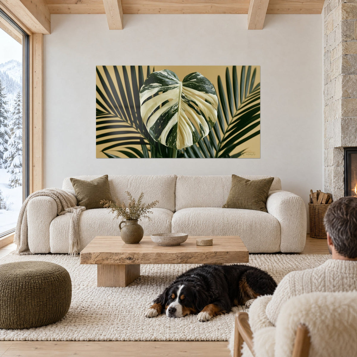 Wall art monstera leaf variegated cream and deep green, ochre background, two people seen from behind and a black dog, above a sofa in a bright living room