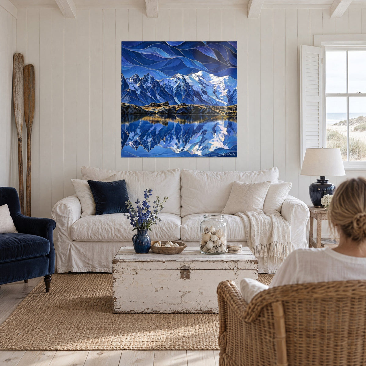 Gemälde eines verschneiten Massivs mit blauen und goldenen Reflexen, spiegelglatter See, über einem Sofa in einem hellen Wohnzimmer
