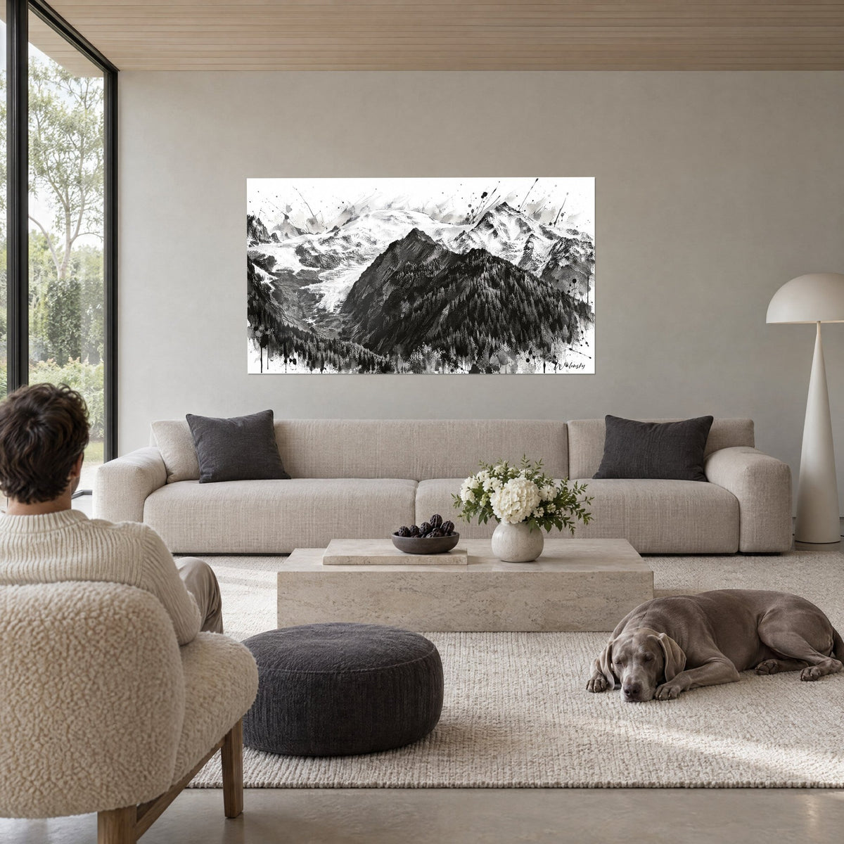 Wall art of a massive rocky peak streaked with black ink, white glacier and dark fir trees, above a sofa in a bright living room