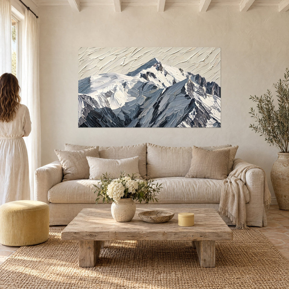 Cuadro macizo montaña nevada con crestas gris azulado y nieve blanco crema en pasta gruesa, pareja de espaldas, sobre un sofá en un salón luminoso
