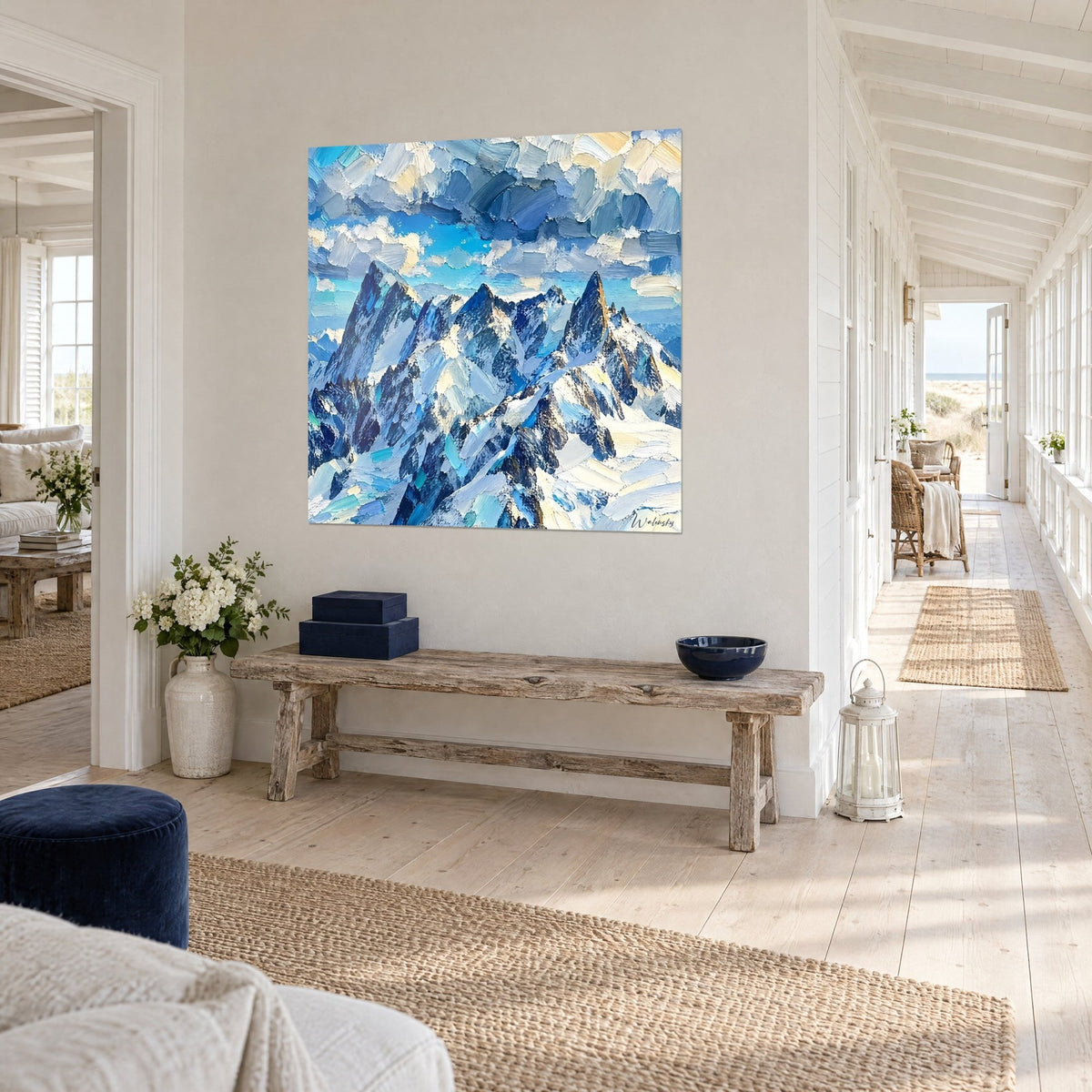 Cuadro montaña nevada maciza en empastes crema y azul glaciar, visto en tres cuartos en un pasillo claro de casa junto al mar