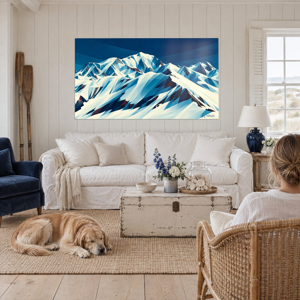 Cuadro cumbres nevadas en facetas azul noche y marfil, cielo marino rayado, retriever tumbado, encima de un sofá en un salón luminoso