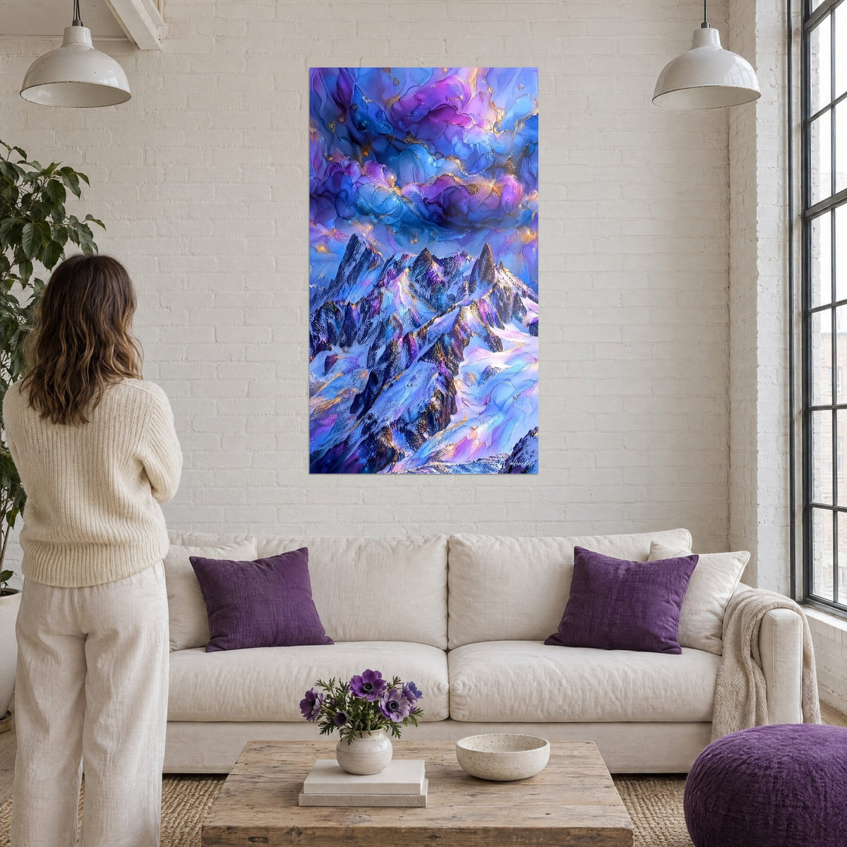 Wall art with jagged alpine peaks under purple and blue clouds, golden glints, above a sofa in a bright living room