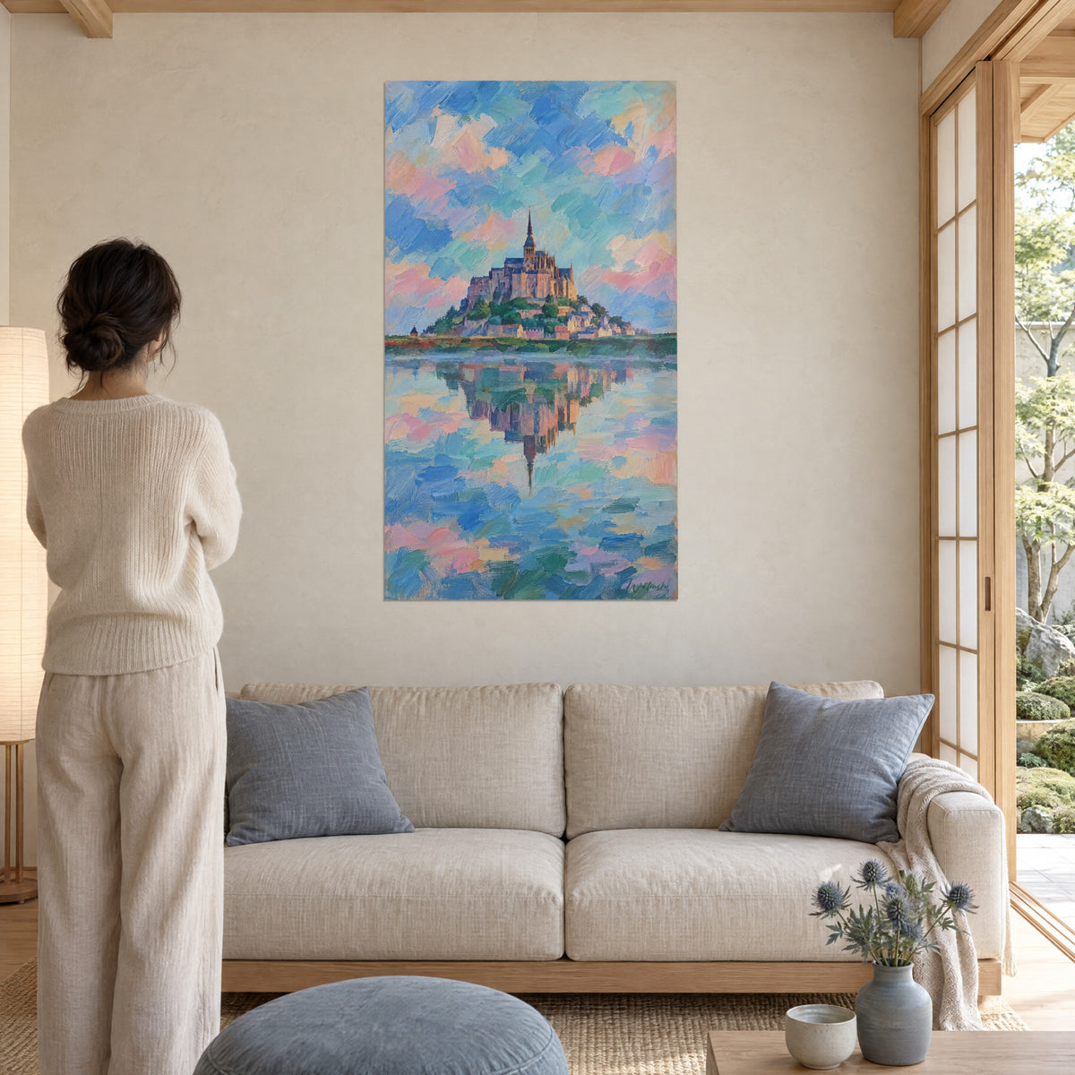 Schilderij abdij met gouden spits op haar rots, blauwe en roze lucht, vrouw van achteren, boven een bank in een lichte woonkamer