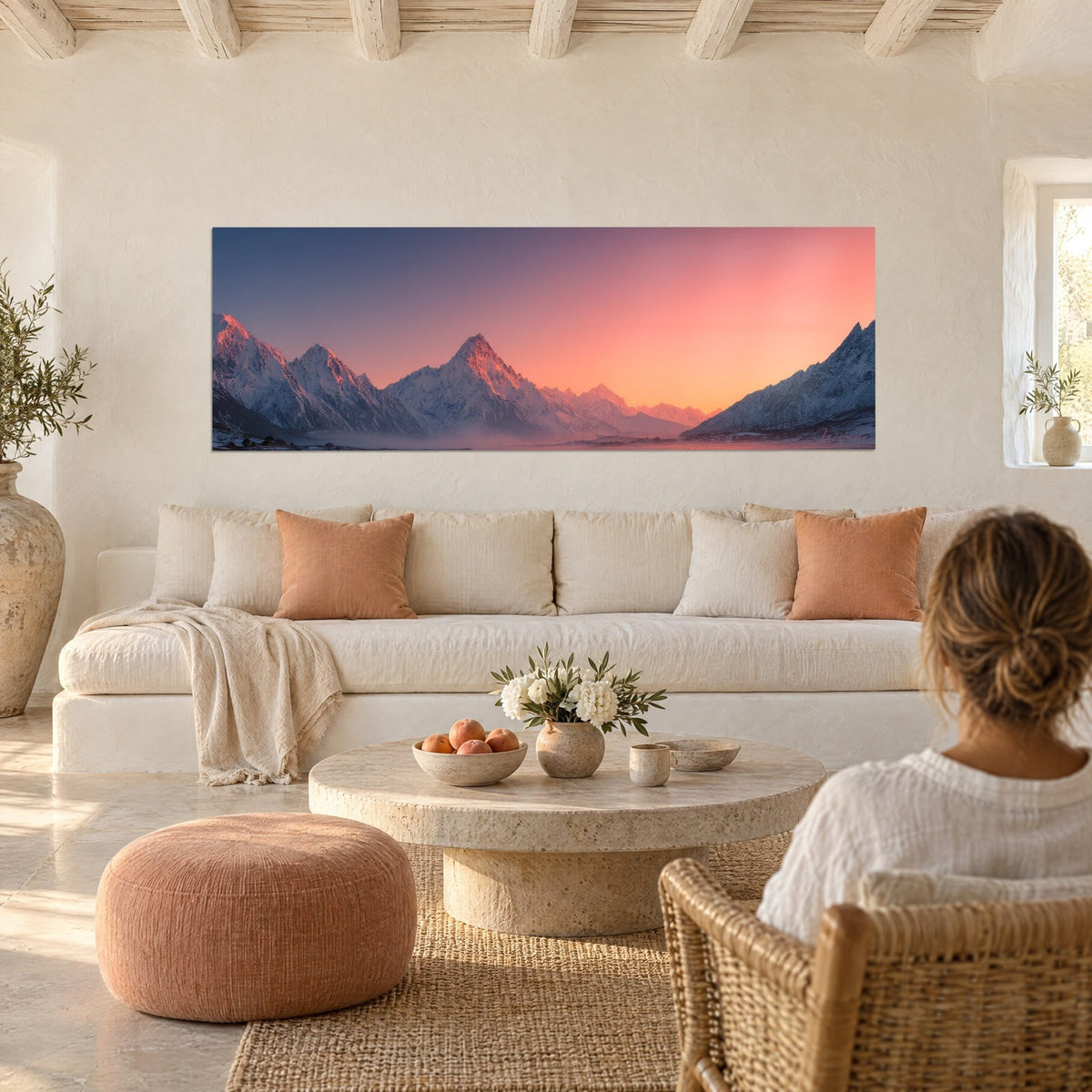 Tableau panorama alpin aux cimes enneigées, ciel rose corail et bleu nuit, au-dessus d'un canapé dans un salon lumineux