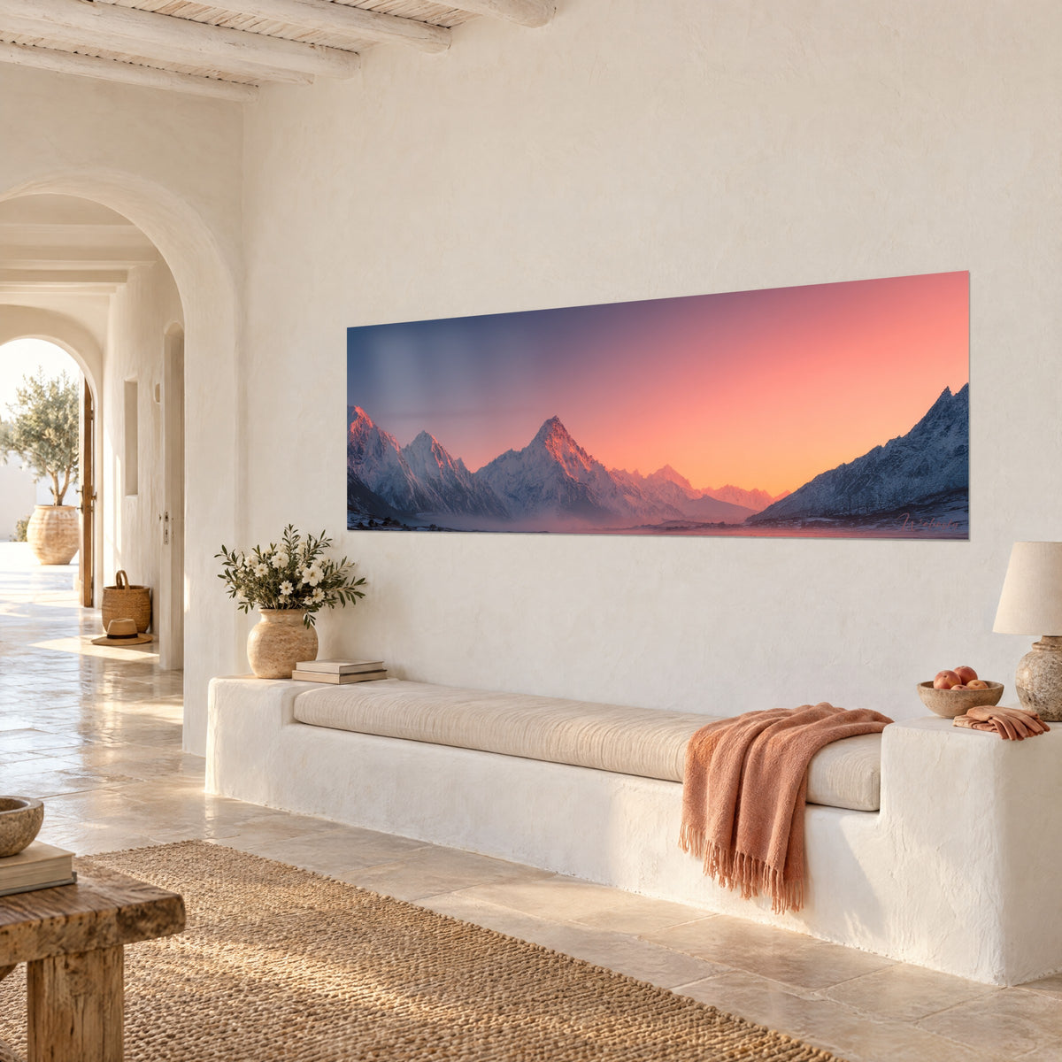Cuadro picos glaciares teñidos de rosa por el amanecer, cielo anaranjado y violeta, colgado en una pared blanca de una casa mediterránea